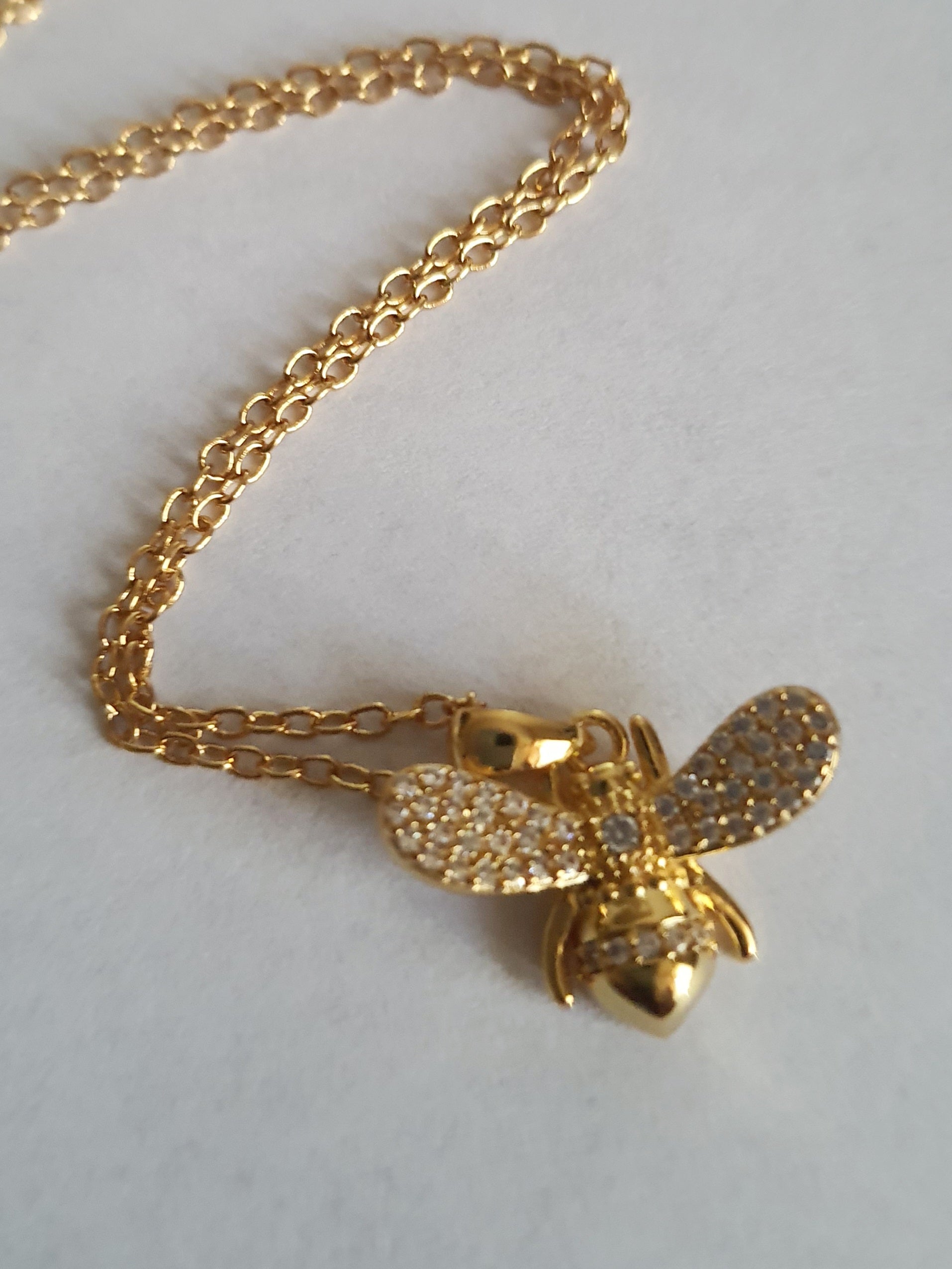 Złoty naszyjnik ze stali chirurgicznej z zawieszką w kształcie pszczółki wysadzanej cyrkoniami. Regulowana długość 40–45 cm. Stal chirurgiczna, stal nierdzewna, wodoodporne, hipoalergiczne, jakość premium. RougeBizu.