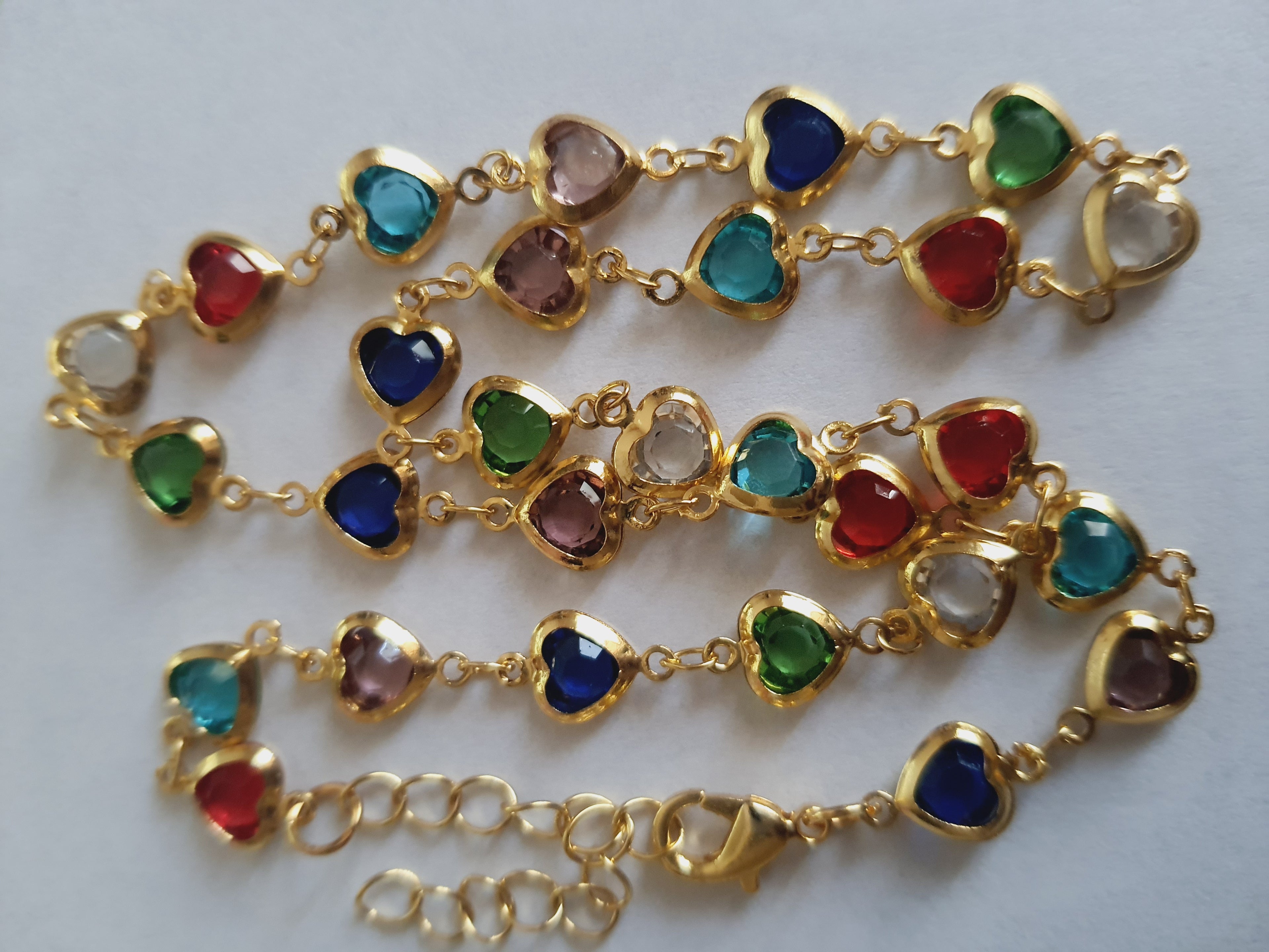 Złoty naszyjnik ze stali chirurgicznej z kolorowymi serduszkami z kryształów w barwach czerwonych, zielonych, niebieskich, fioletowych i turkusowych. Regulowana długość 40–45 cm. Stal chirurgiczna, stal nierdzewna, wodoodporne, hipoalergiczne, jakość premium. RougeBizu.