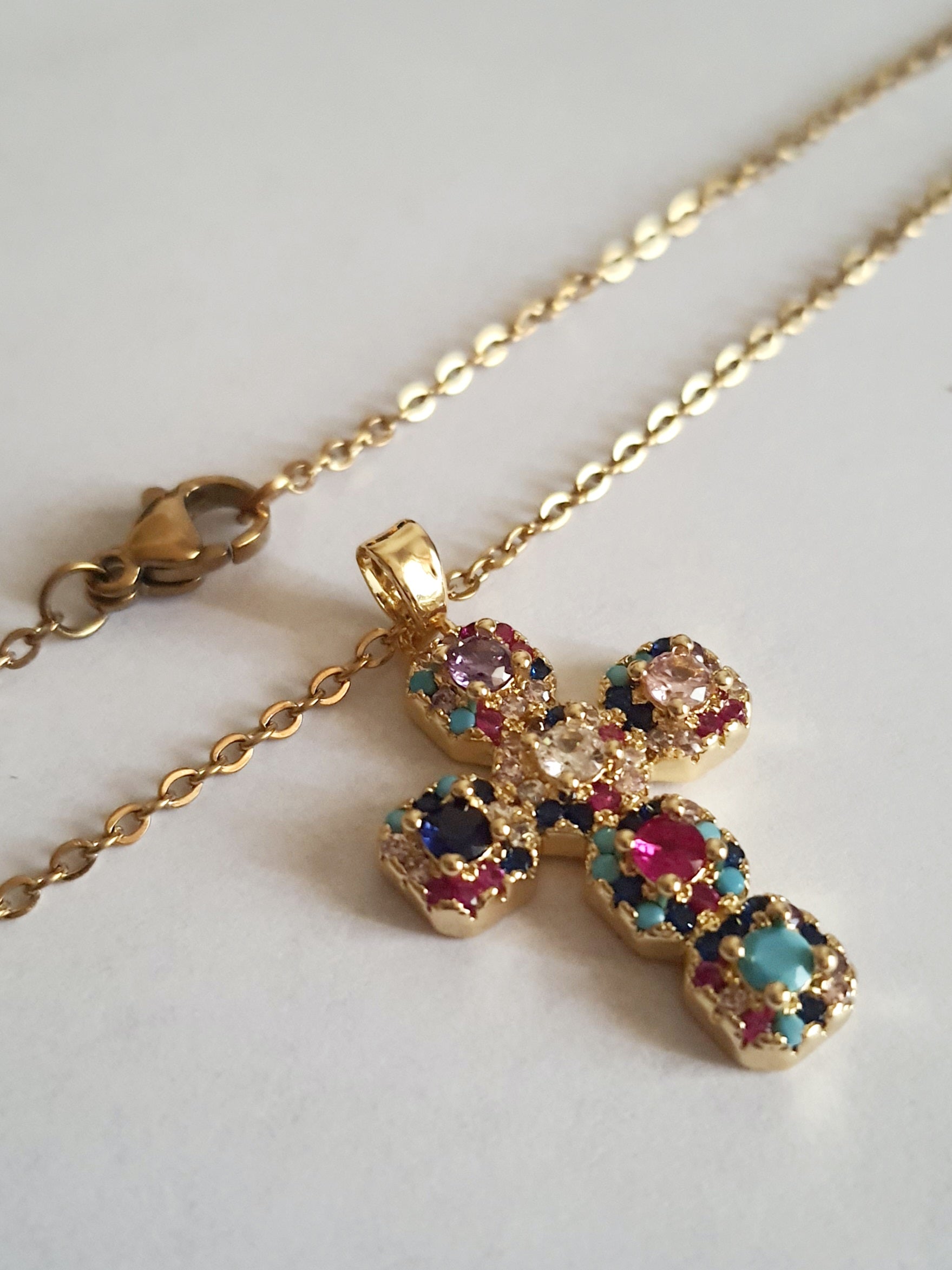Złoty naszyjnik ze stali chirurgicznej z zawieszką w kształcie krzyża wysadzanego kolorowymi kryształami (czerwonymi, niebieskimi, fioletowymi, turkusowymi). Długość łańcuszka 50 cm. Stal chirurgiczna, stal nierdzewna, wodoodporne, hipoalergiczne, jakość premium. RougeBizu.