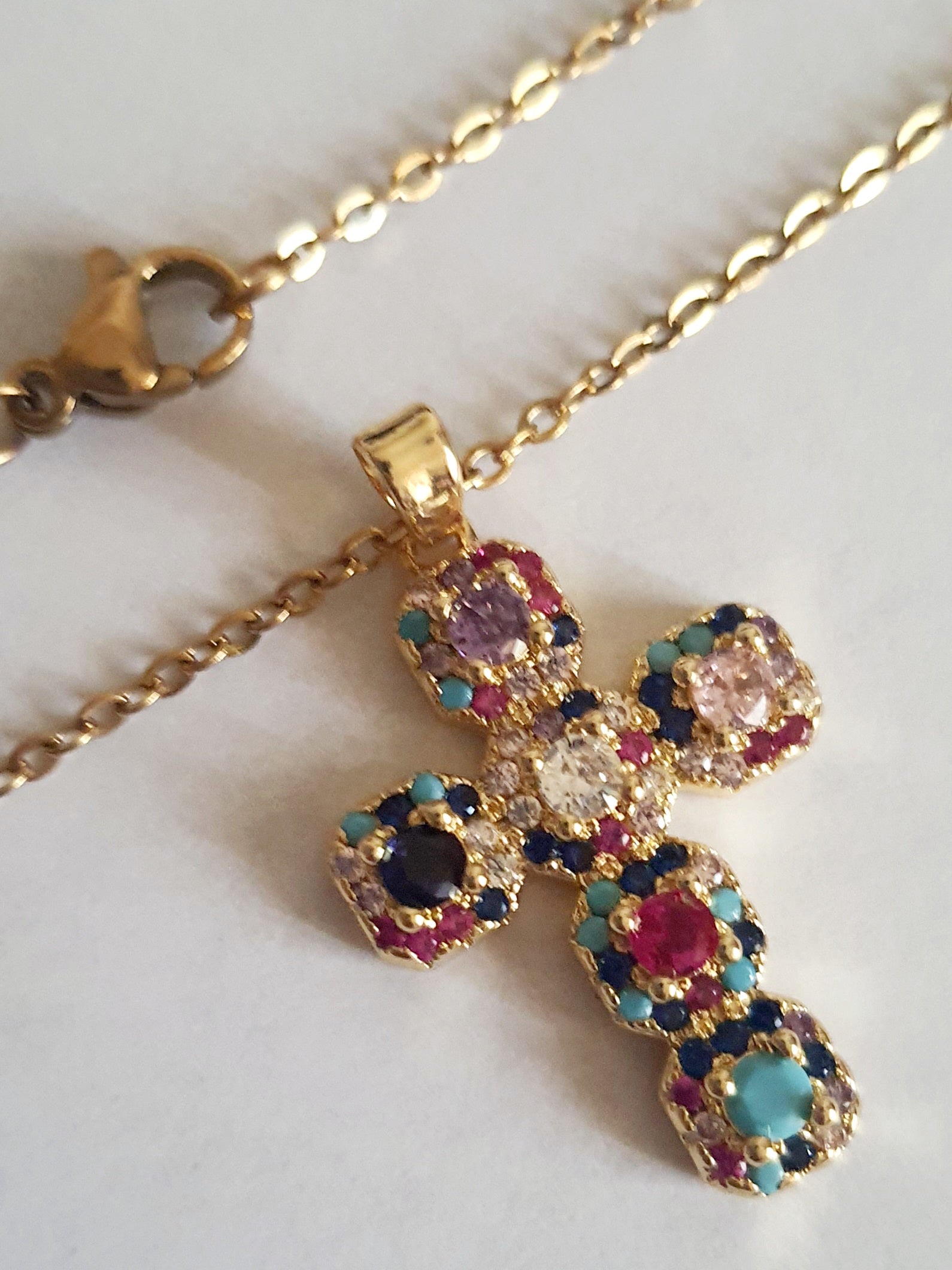 Złoty naszyjnik ze stali chirurgicznej z zawieszką w kształcie krzyża wysadzanego kolorowymi kryształami (czerwonymi, niebieskimi, fioletowymi, turkusowymi). Długość łańcuszka 50 cm. Stal chirurgiczna, stal nierdzewna, wodoodporne, hipoalergiczne, jakość premium. RougeBizu.