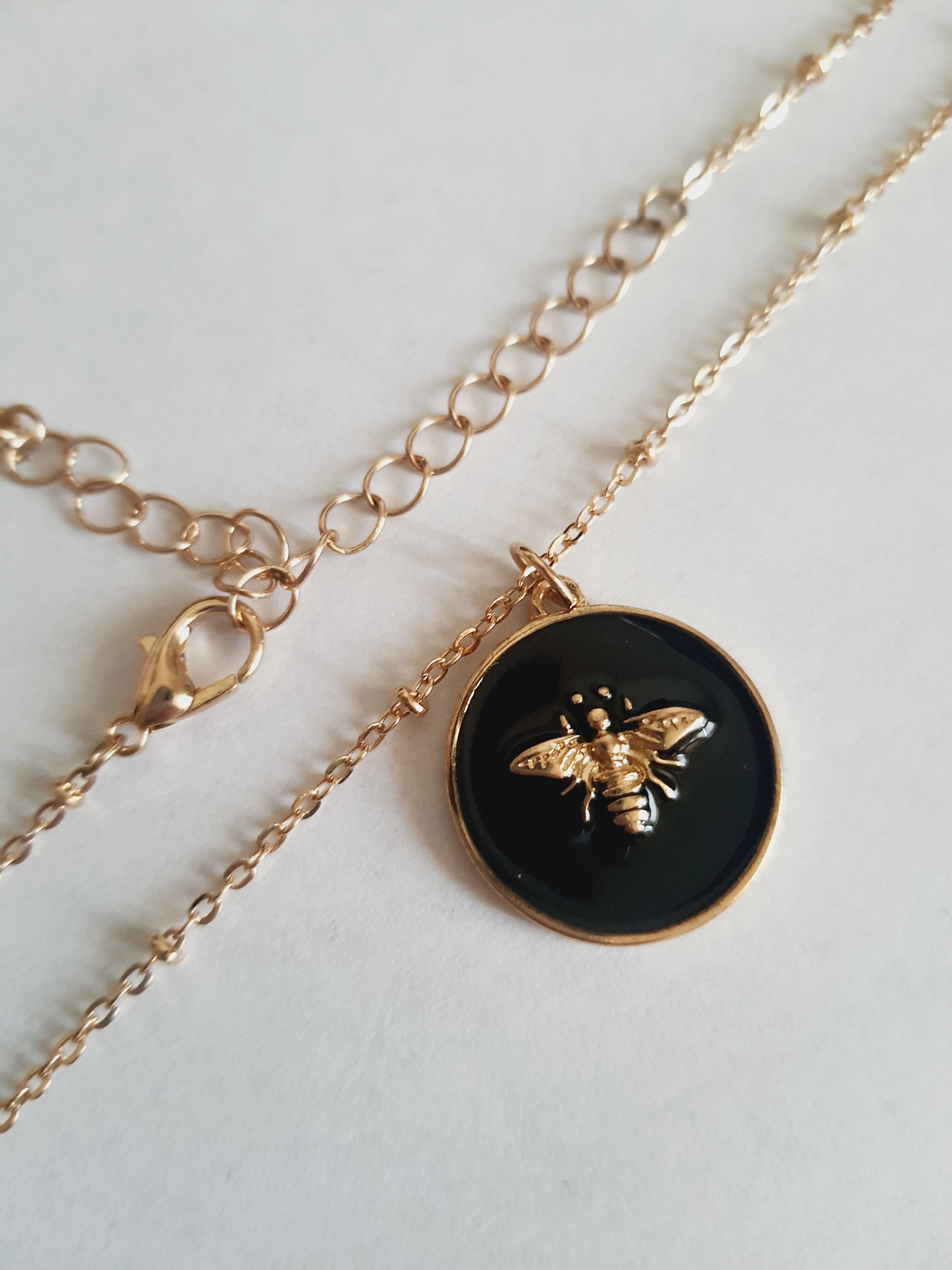 Złoty naszyjnik ze stali chirurgicznej z czarną okrągłą zawieszką i złotą pszczółką. Regulowana długość 40–49 cm. Stal chirurgiczna, stal nierdzewna, wodoodporne, hipoalergiczne, jakość premium. RougeBizu.