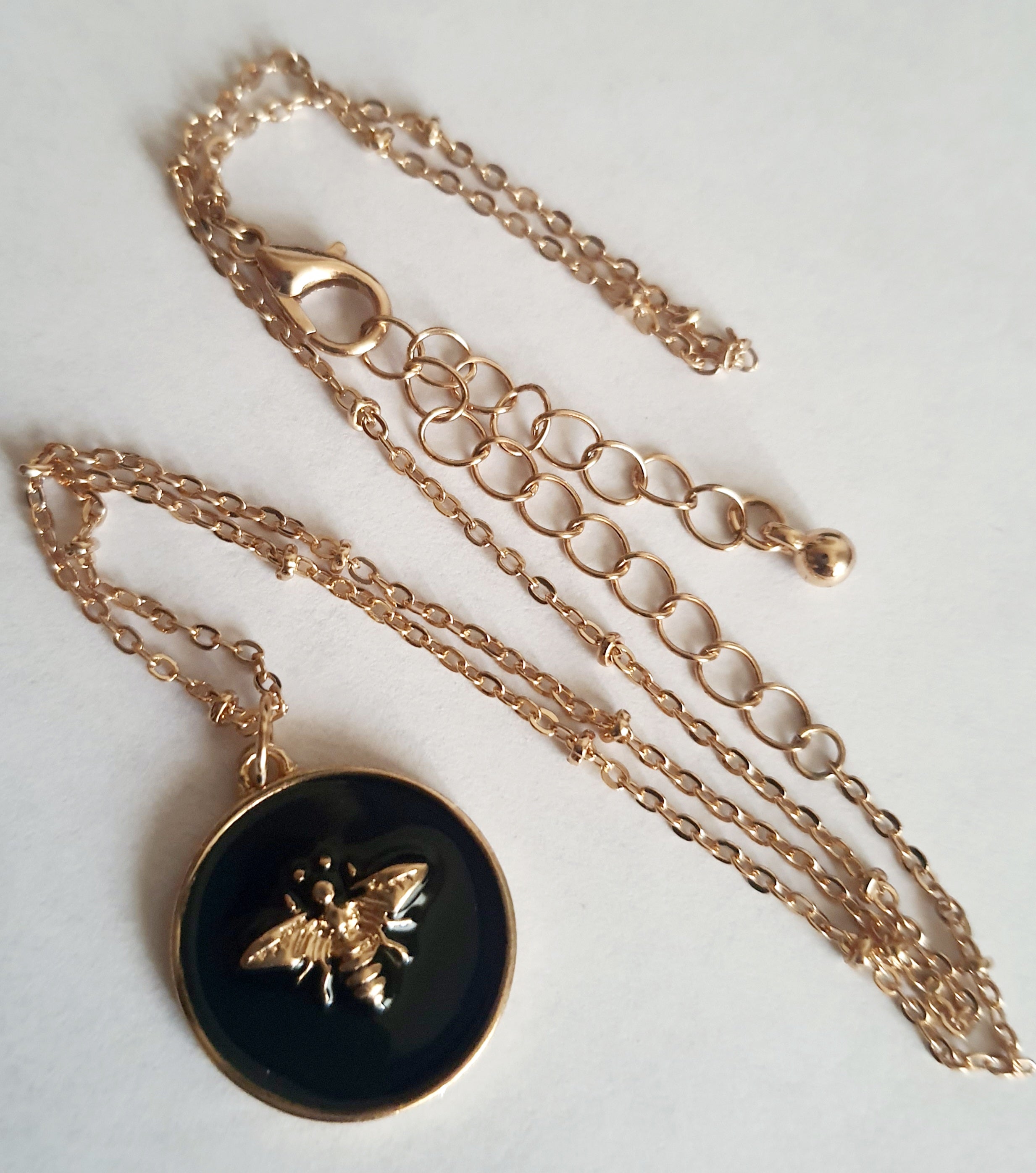 Złoty naszyjnik ze stali chirurgicznej z czarną okrągłą zawieszką i złotą pszczółką. Regulowana długość 40–49 cm. Stal chirurgiczna, stal nierdzewna, wodoodporne, hipoalergiczne, jakość premium. RougeBizu.