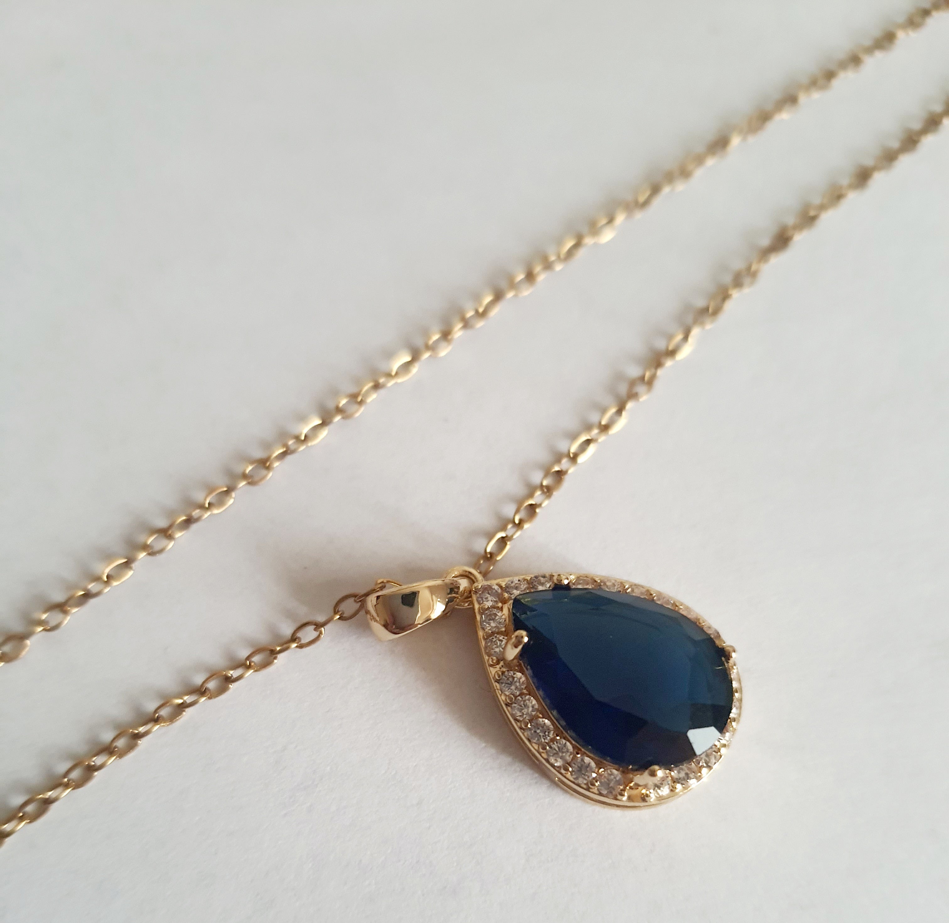 Złoty naszyjnik ze stali chirurgicznej z zawieszką w kształcie łezki z granatowym kamieniem otoczonym cyrkoniami. Regulowana długość 41–47 cm. Stal chirurgiczna, stal nierdzewna, wodoodporne, hipoalergiczne, jakość premium. RougeBizu.