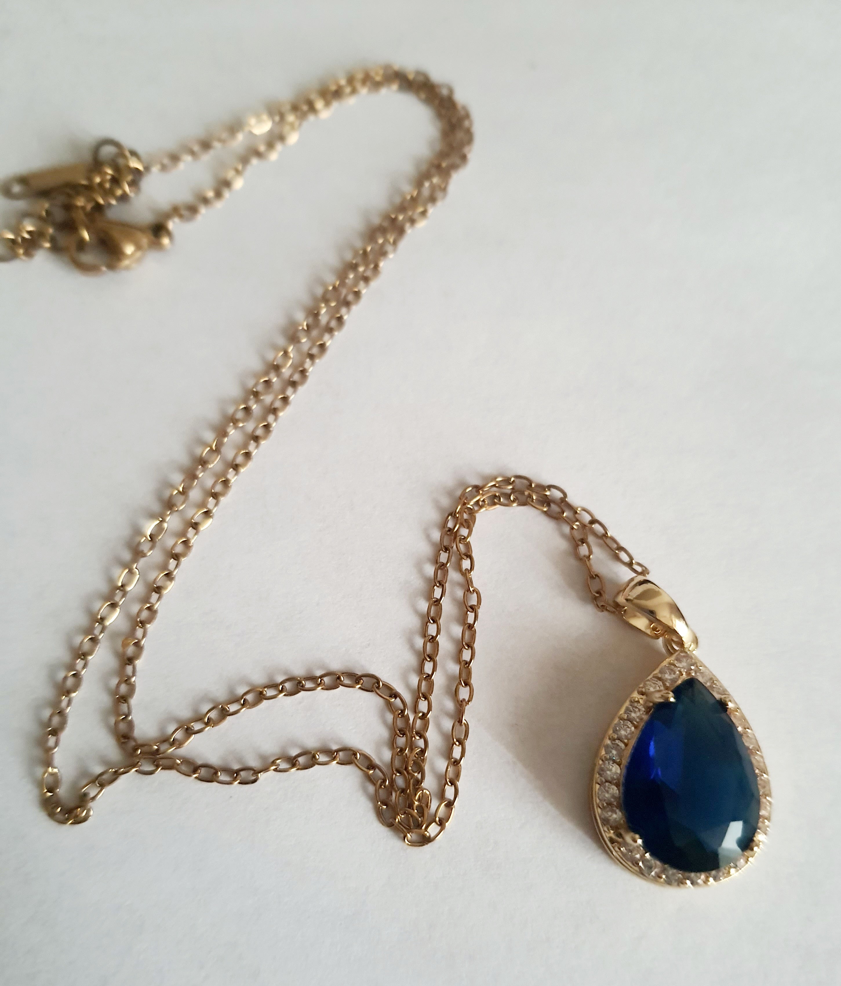 Złoty naszyjnik ze stali chirurgicznej z zawieszką w kształcie łezki z granatowym kamieniem otoczonym cyrkoniami. Regulowana długość 41–47 cm. Stal chirurgiczna, stal nierdzewna, wodoodporne, hipoalergiczne, jakość premium. RougeBizu.