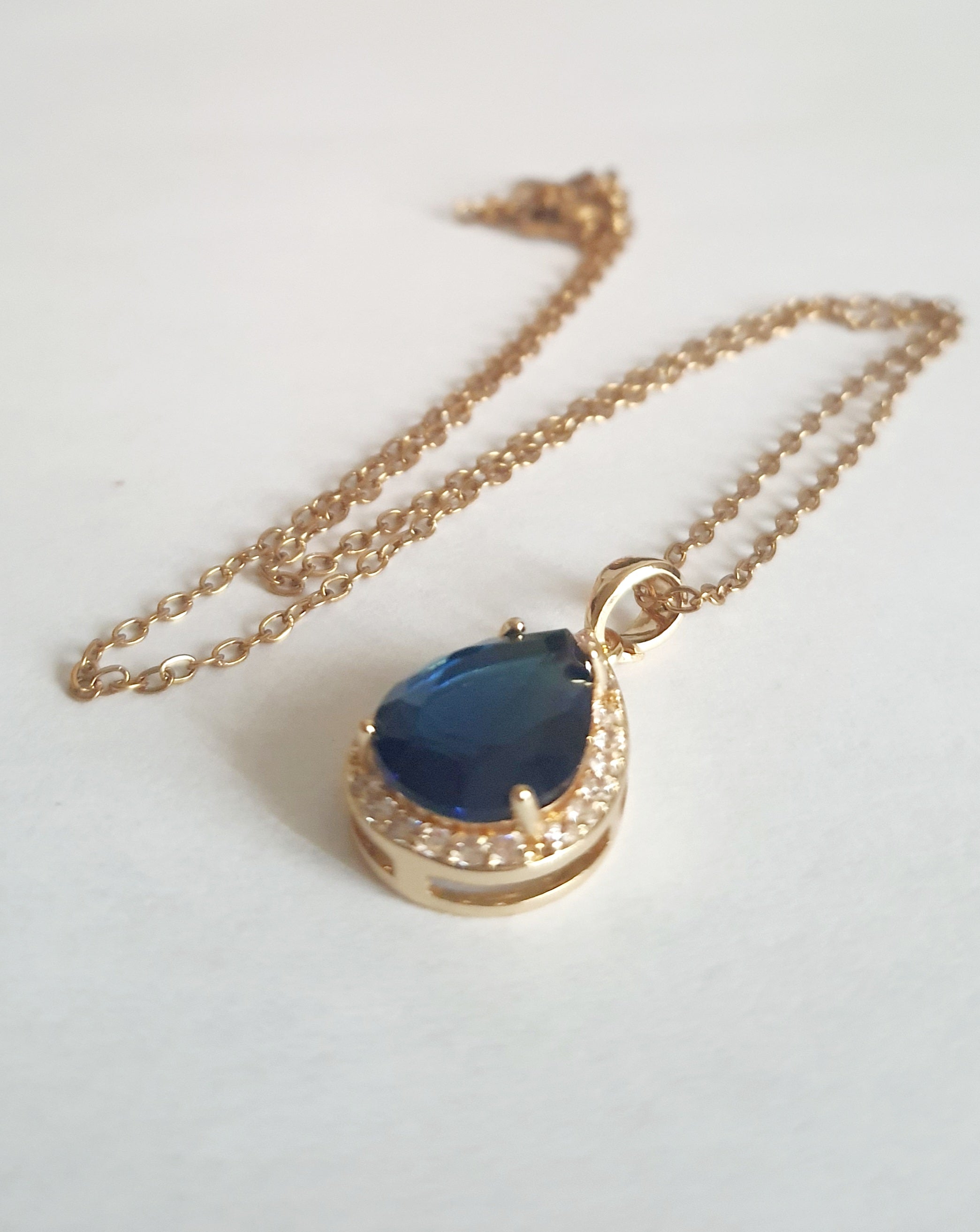 Złoty naszyjnik ze stali chirurgicznej z zawieszką w kształcie łezki z granatowym kamieniem otoczonym cyrkoniami. Regulowana długość 41–47 cm. Stal chirurgiczna, stal nierdzewna, wodoodporne, hipoalergiczne, jakość premium. RougeBizu.