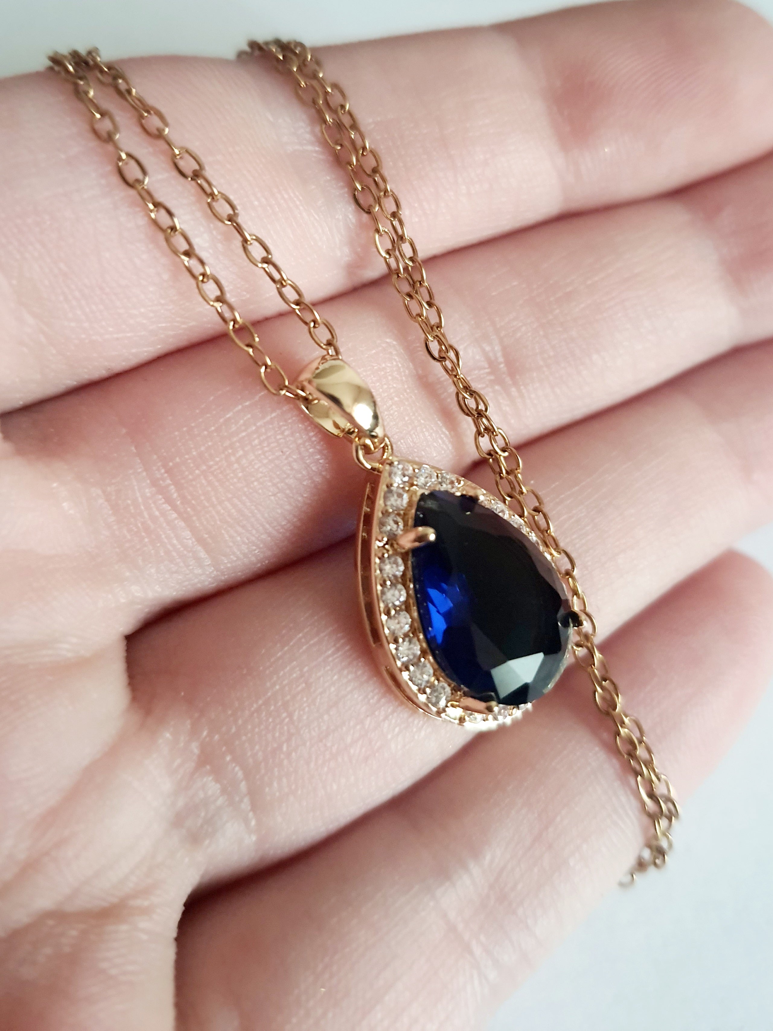 Złoty naszyjnik ze stali chirurgicznej z zawieszką w kształcie łezki z granatowym kamieniem otoczonym cyrkoniami. Regulowana długość 41–47 cm. Stal chirurgiczna, stal nierdzewna, wodoodporne, hipoalergiczne, jakość premium. RougeBizu.