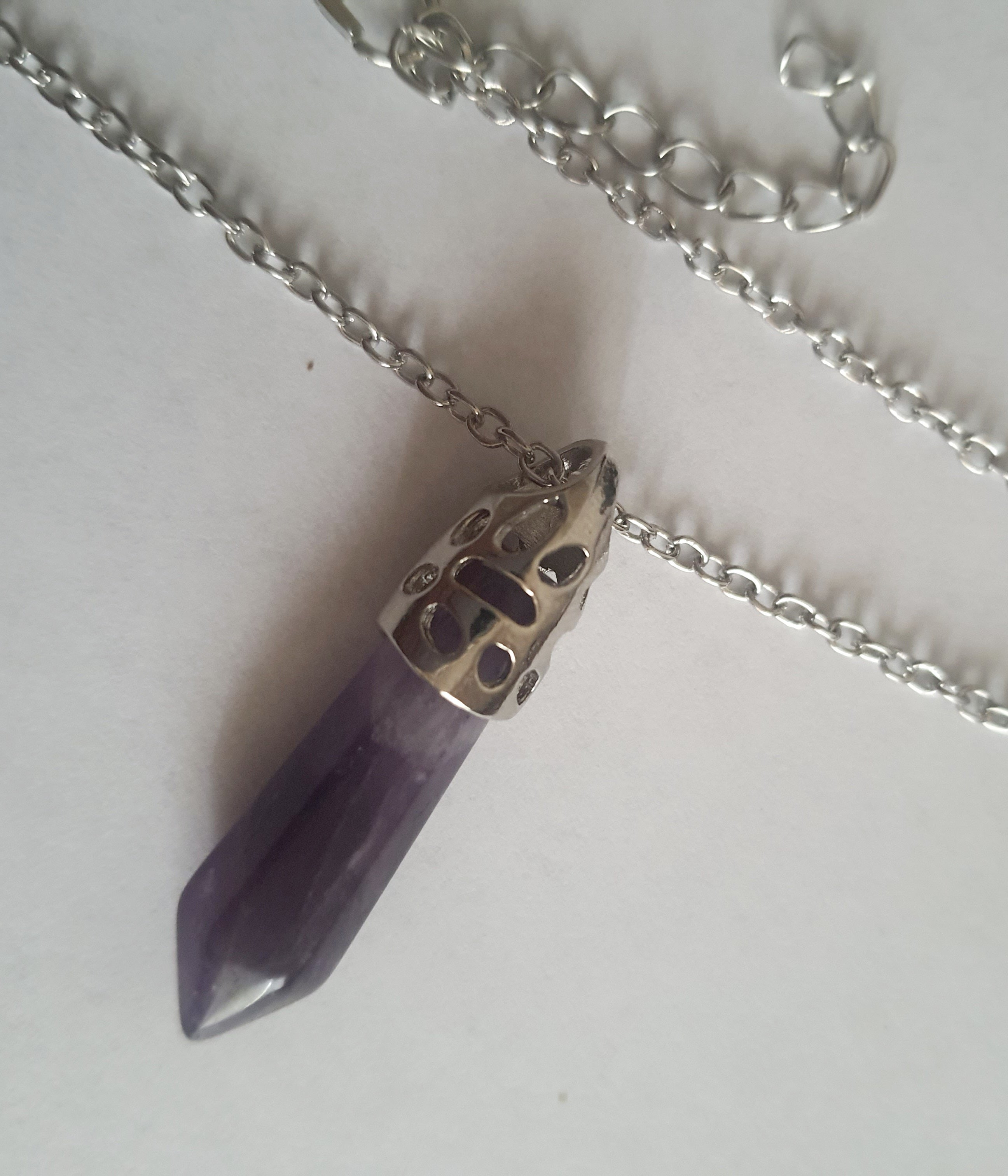 Srebrny naszyjnik ze stali chirurgicznej z zawieszką w postaci syntetycznego ametystu w kształcie szpica. Regulowana długość 48–52 cm. Stal chirurgiczna, stal nierdzewna, wodoodporne, hipoalergiczne, jakość premium. RougeBizu.