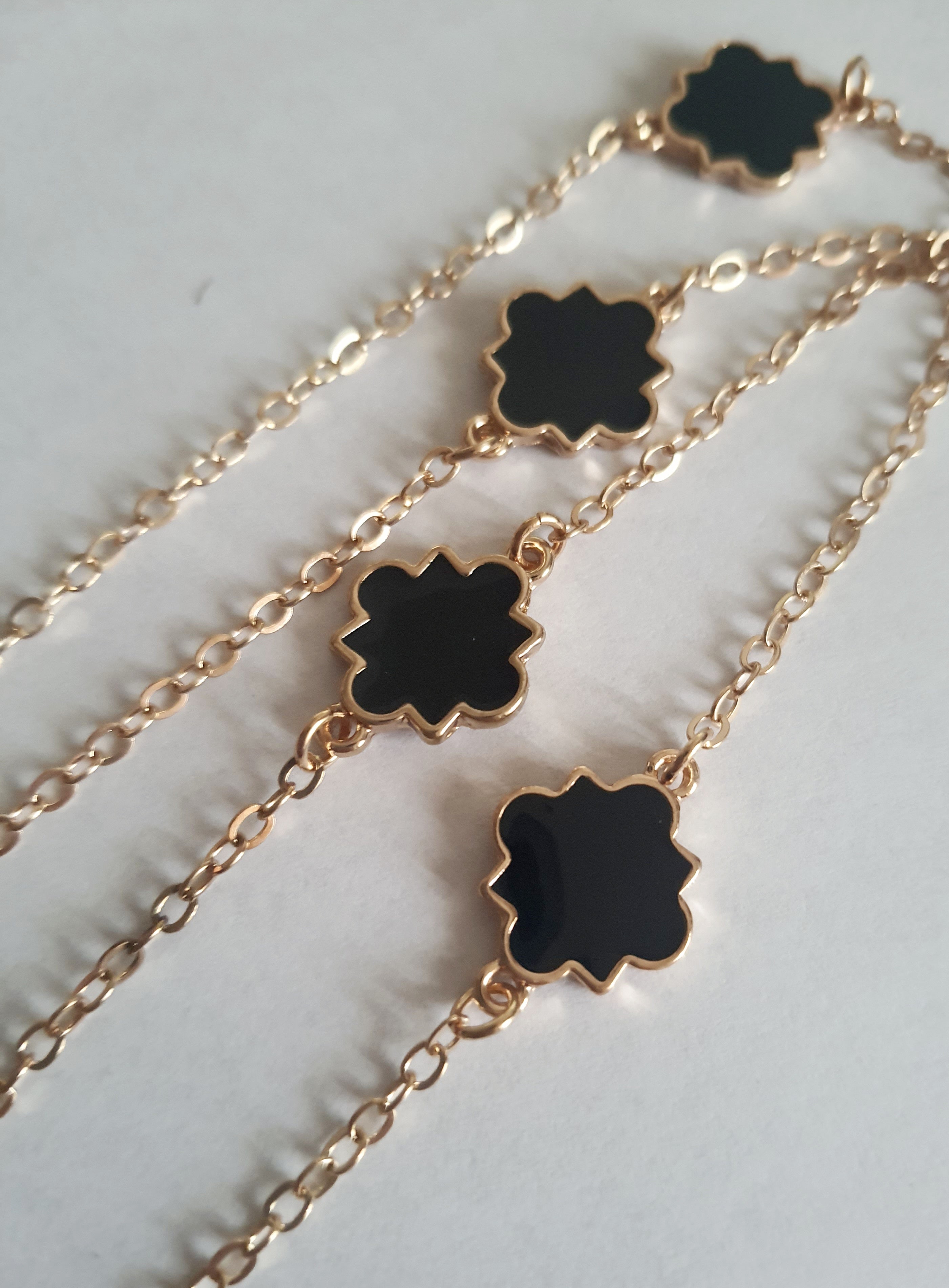 Długi złoty naszyjnik ze stali chirurgicznej z czarnymi zawieszkami w kształcie czterolistnych motywów. Regulowana długość 83–90 cm. Stal chirurgiczna, stal nierdzewna, wodoodporne, hipoalergiczne, jakość premium. RougeBizu.