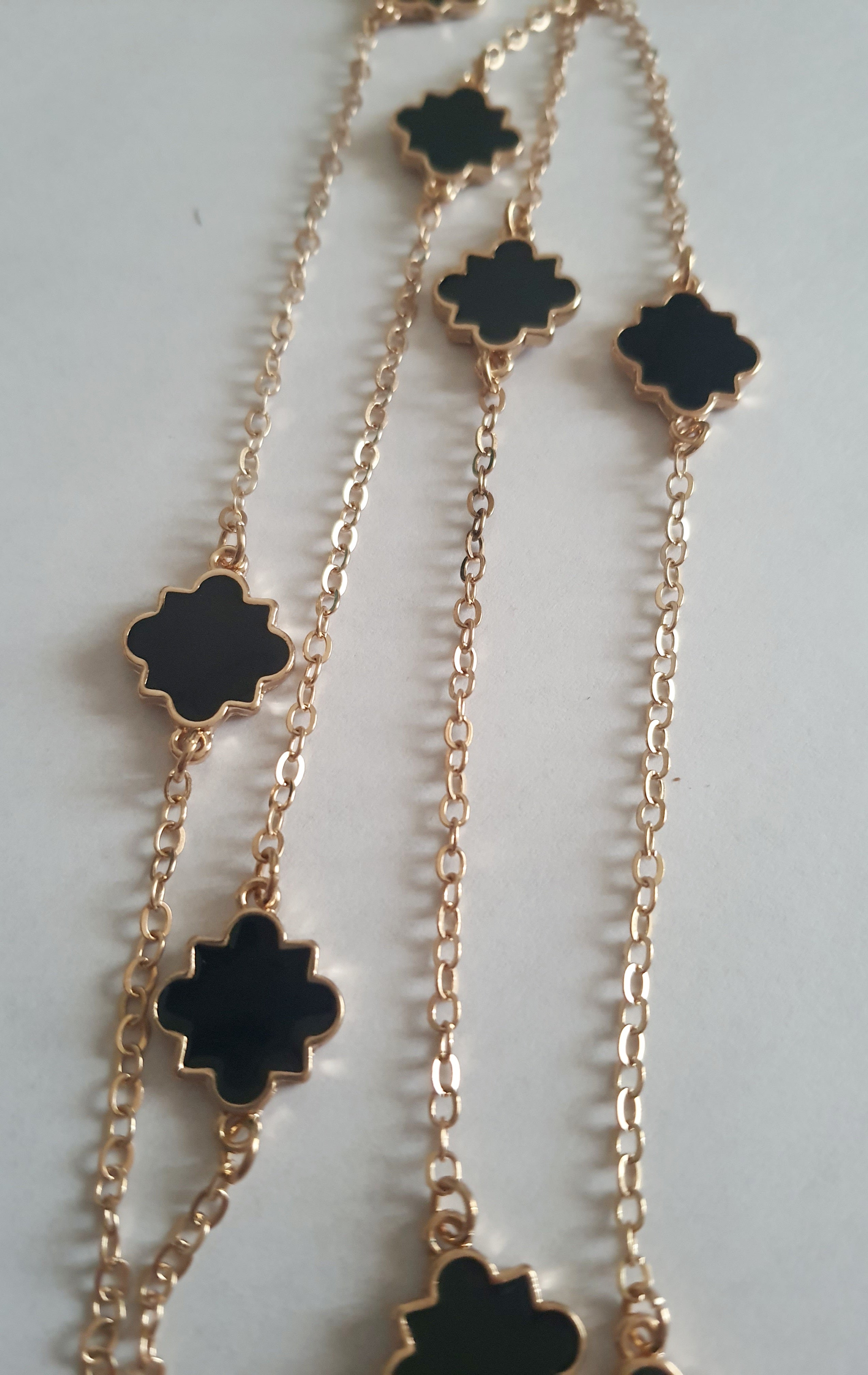 Długi złoty naszyjnik ze stali chirurgicznej z czarnymi zawieszkami w kształcie czterolistnych motywów. Regulowana długość 83–90 cm. Stal chirurgiczna, stal nierdzewna, wodoodporne, hipoalergiczne, jakość premium. RougeBizu.v
