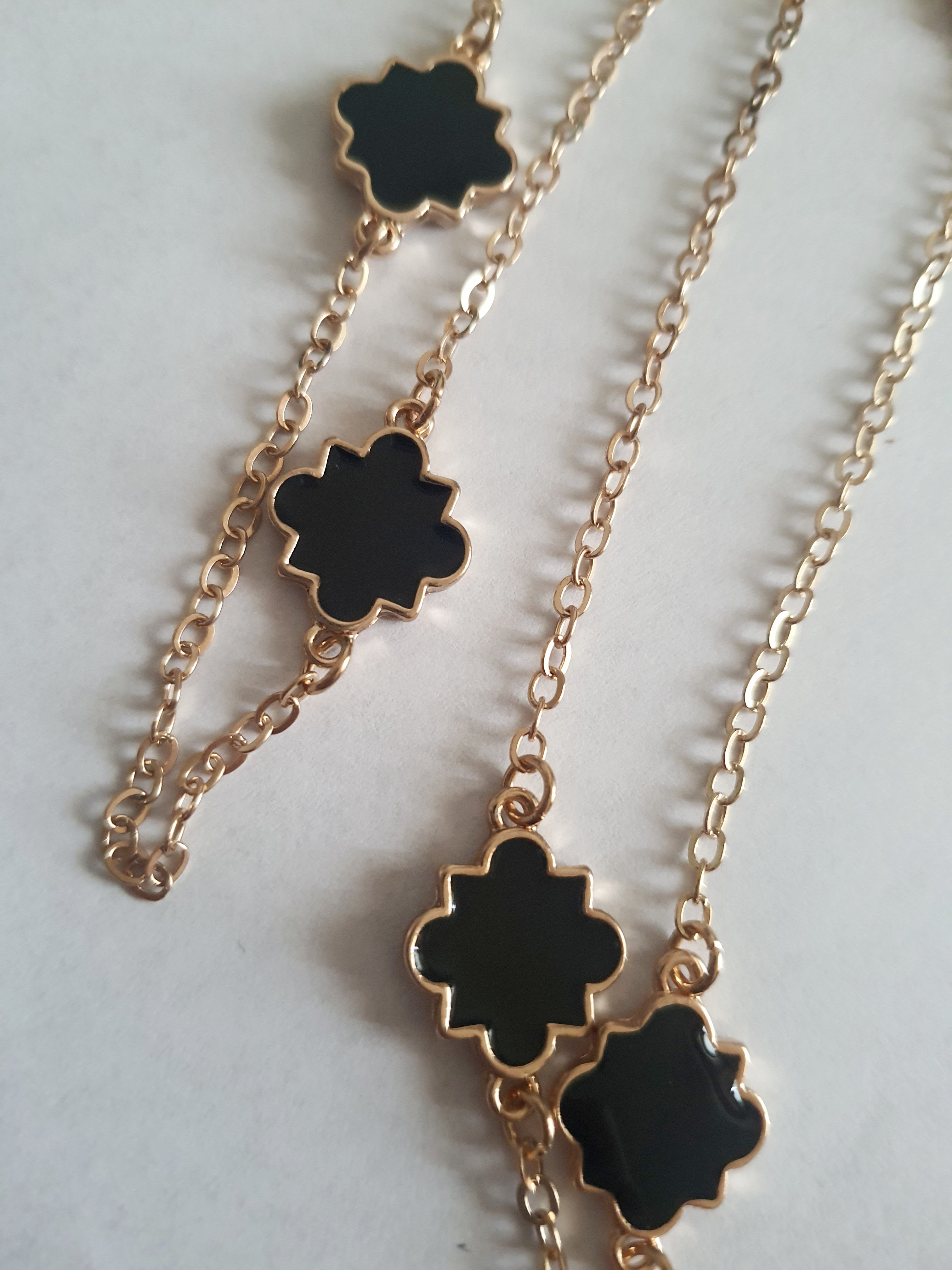 Długi złoty naszyjnik ze stali chirurgicznej z czarnymi zawieszkami w kształcie czterolistnych motywów. Regulowana długość 83–90 cm. Stal chirurgiczna, stal nierdzewna, wodoodporne, hipoalergiczne, jakość premium. RougeBizu.