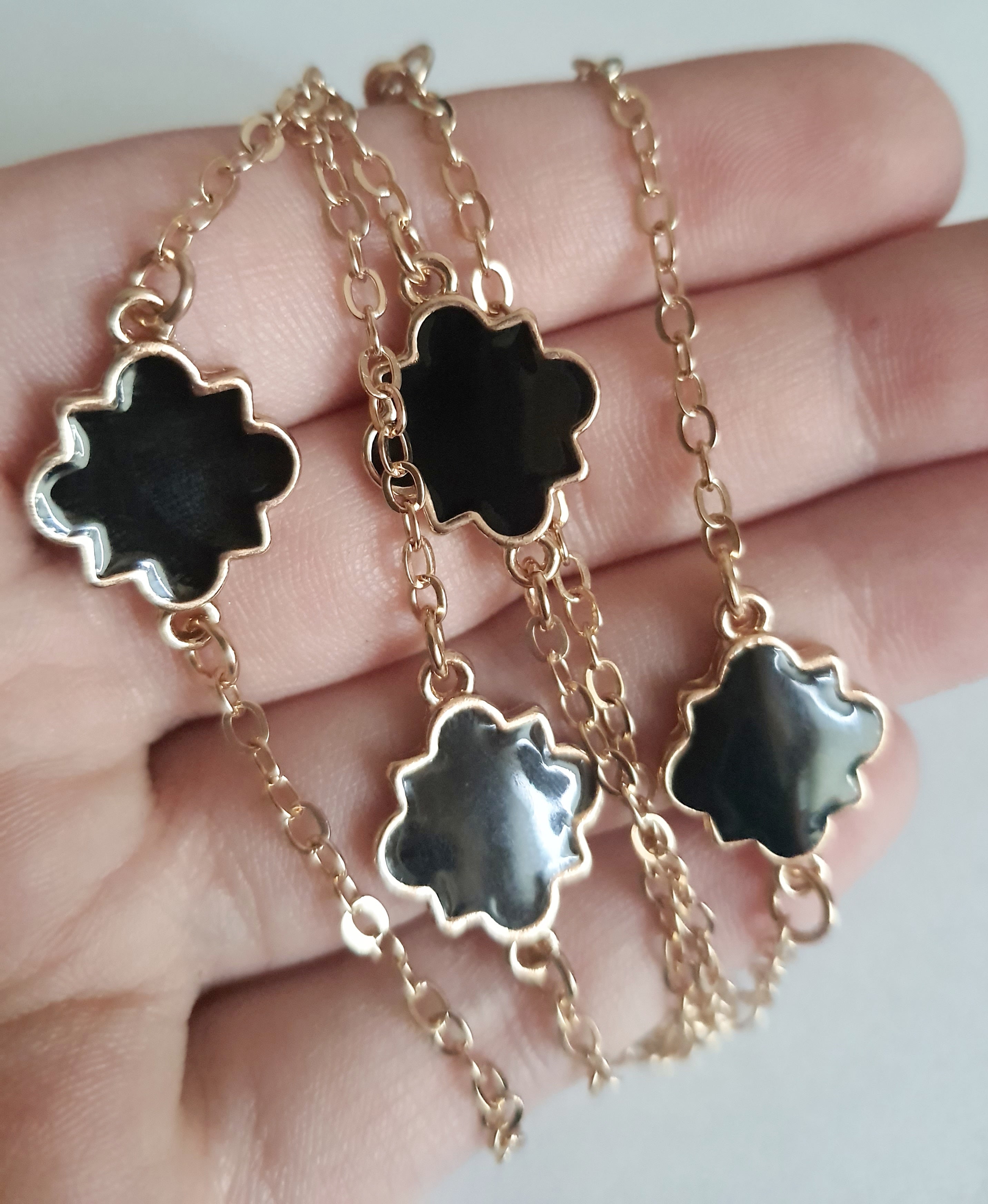 Długi złoty naszyjnik ze stali chirurgicznej z czarnymi zawieszkami w kształcie czterolistnych motywów. Regulowana długość 83–90 cm. Stal chirurgiczna, stal nierdzewna, wodoodporne, hipoalergiczne, jakość premium. RougeBizu.