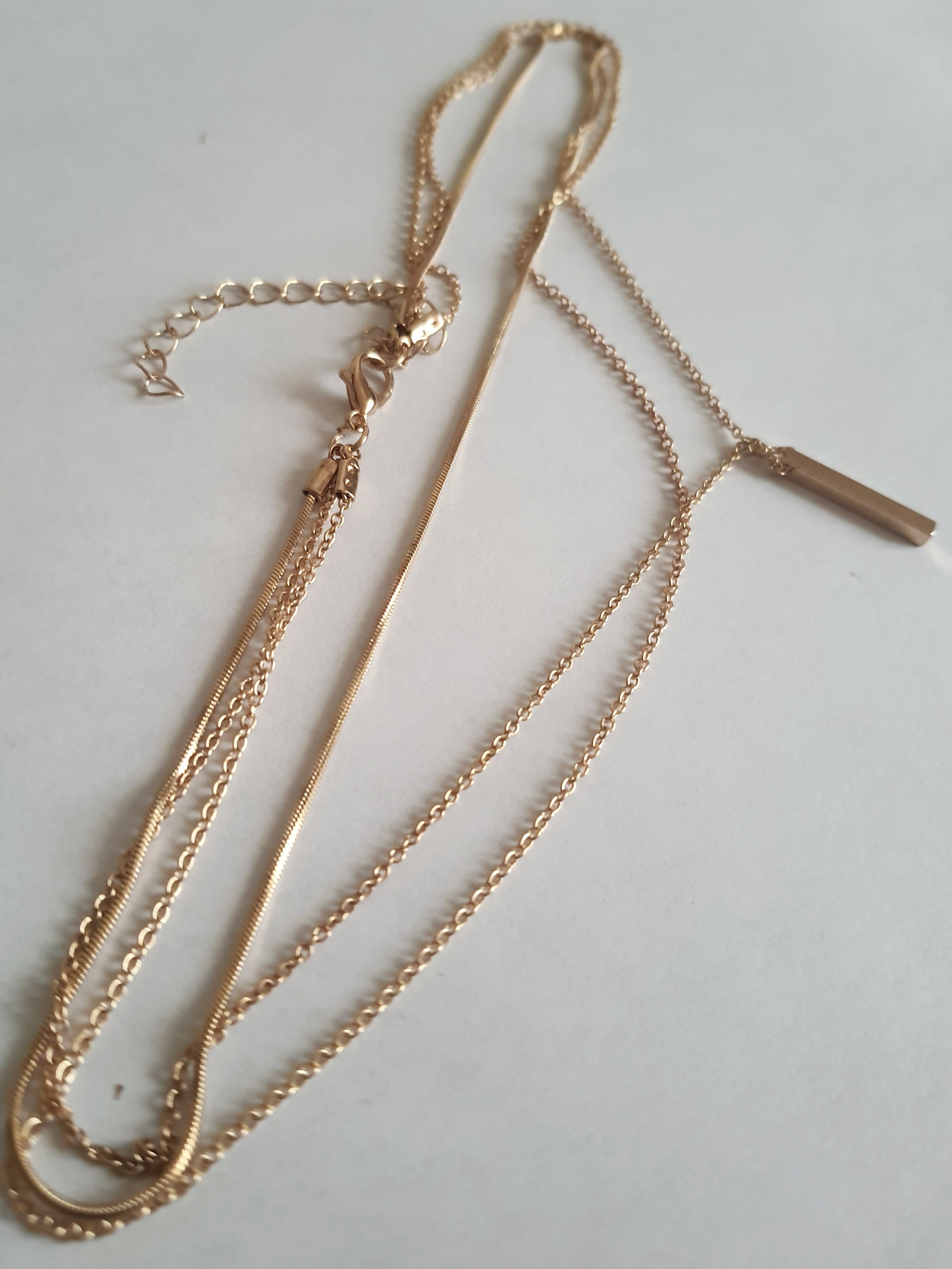 Złoty potrójny naszyjnik ze stali chirurgicznej z delikatnymi łańcuszkami i minimalistycznymi zawieszkami. Regulowana długość 39–45 cm. Stal chirurgiczna, stal nierdzewna, wodoodporne, hipoalergiczne, jakość premium. RougeBizu.