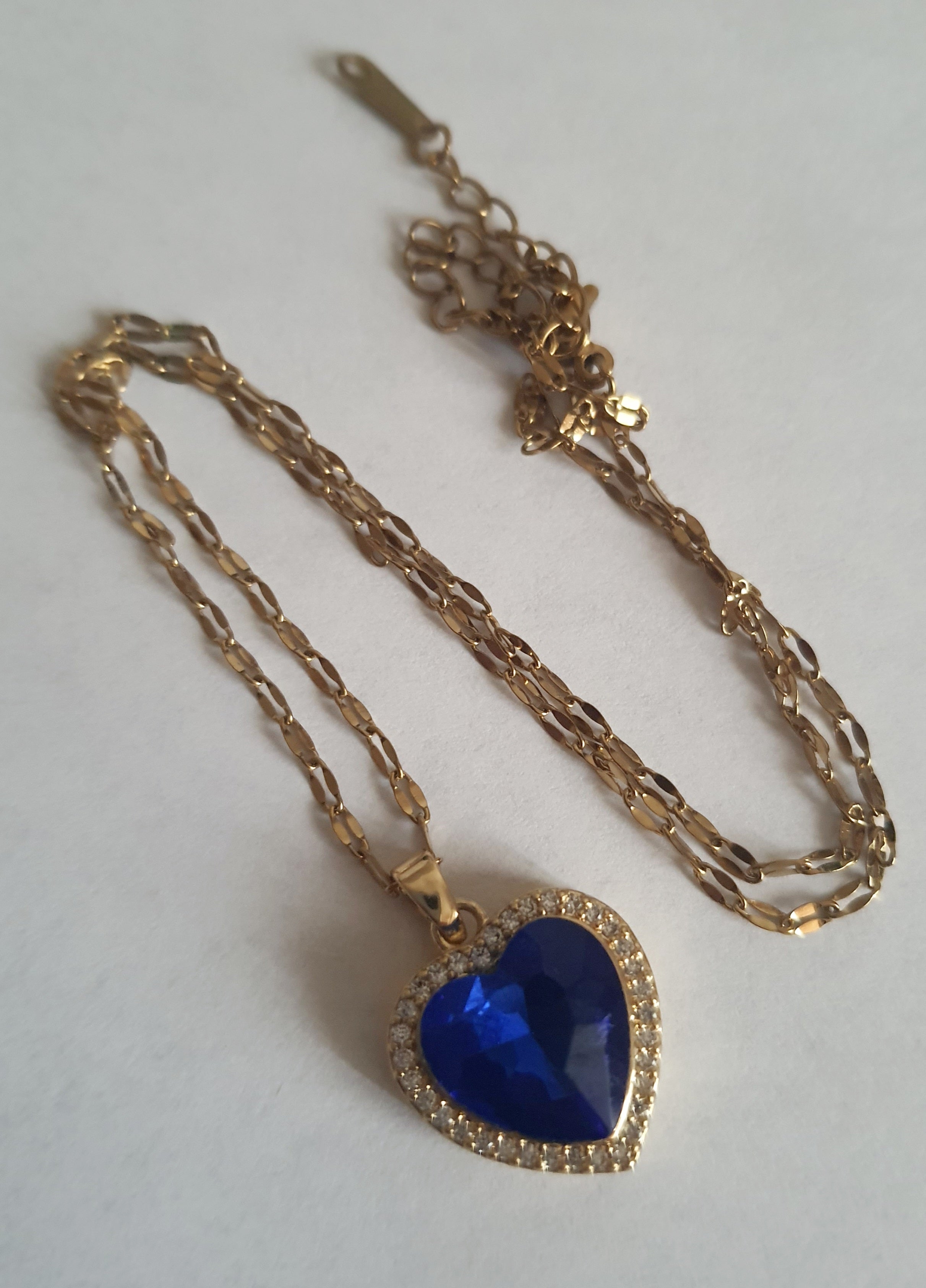 Naszyjnik złoty ze stali nierdzewnej – stal chirurgiczna, wodoodporny, hipoalergiczny, jakość premium. Zawieszka w kształcie serca w kolorze szafirowego błękitu, otoczona drobnymi cyrkoniami. Długość łańcuszka 40–45 cm. Elegancja i styl RougeBizu.