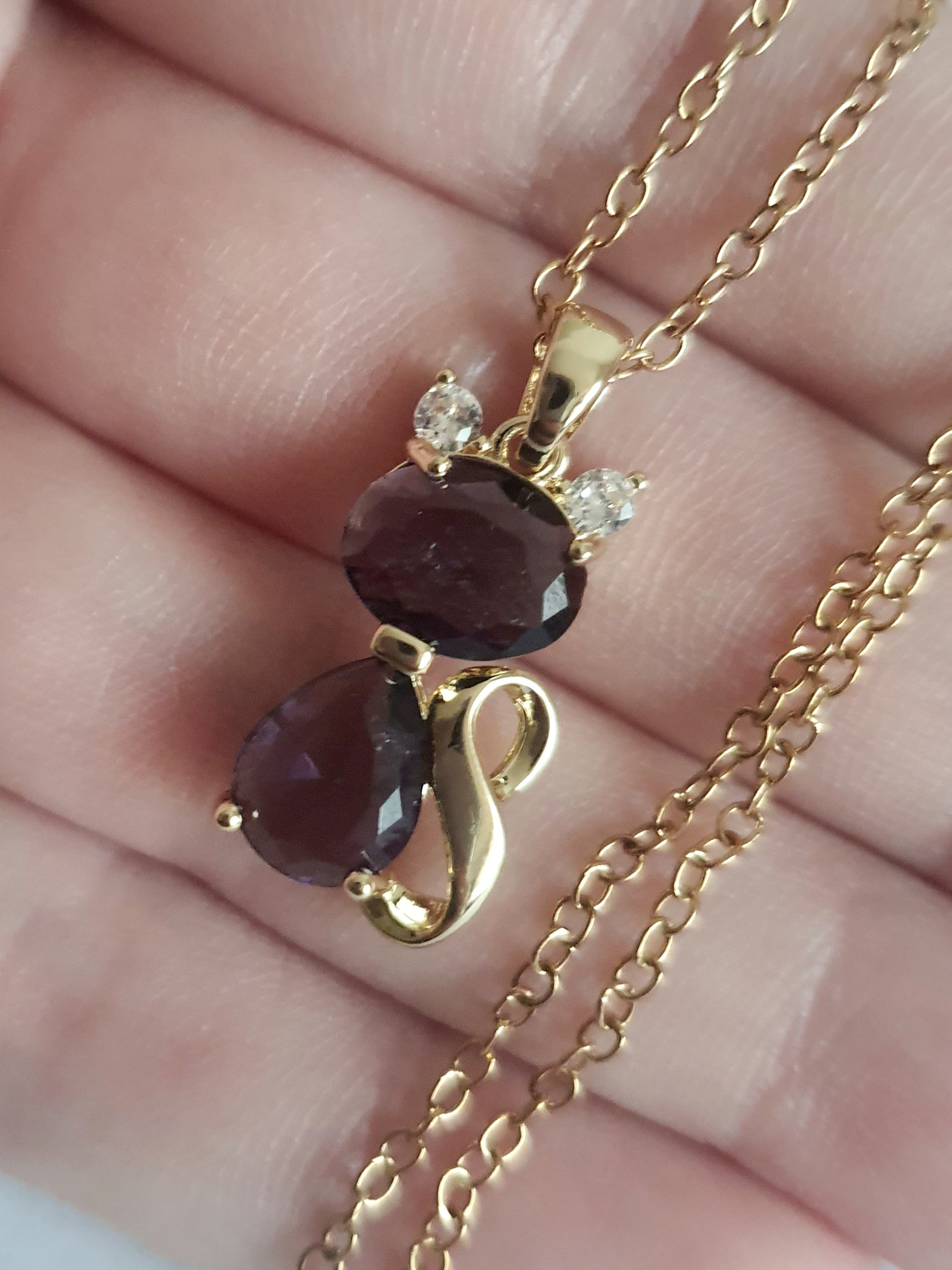 Naszyjnik złoty ze stali nierdzewnej – stal chirurgiczna, wodoodporny, hipoalergiczny, jakość premium. Zawieszka w kształcie kotka z dwóch fioletowych kryształów, ozdobiona złotym detalem i drobnymi cyrkoniami. Długość łańcuszka 40–45 cm. Elegancja i styl RougeBizu.