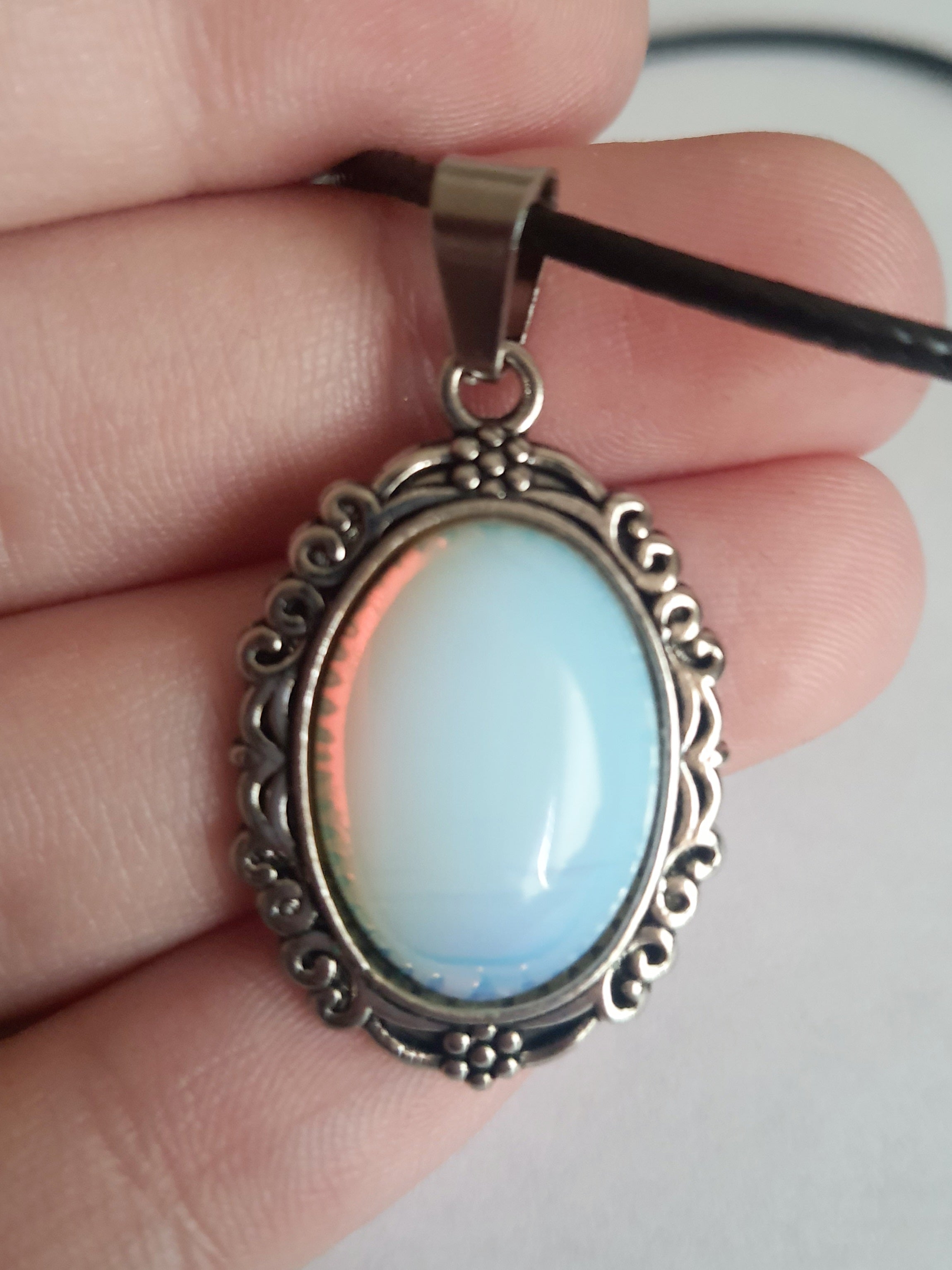 Naszyjnik vintage ze stali nierdzewnej – stal chirurgiczna, wodoodporny, hipoalergiczny, jakość premium. Zawieszka owalna z syntetycznym opalem opalizującym błękitem i bielą, w zdobionej ramie. Czarna linka o długości 45–50 cm. Styl RougeBizu.