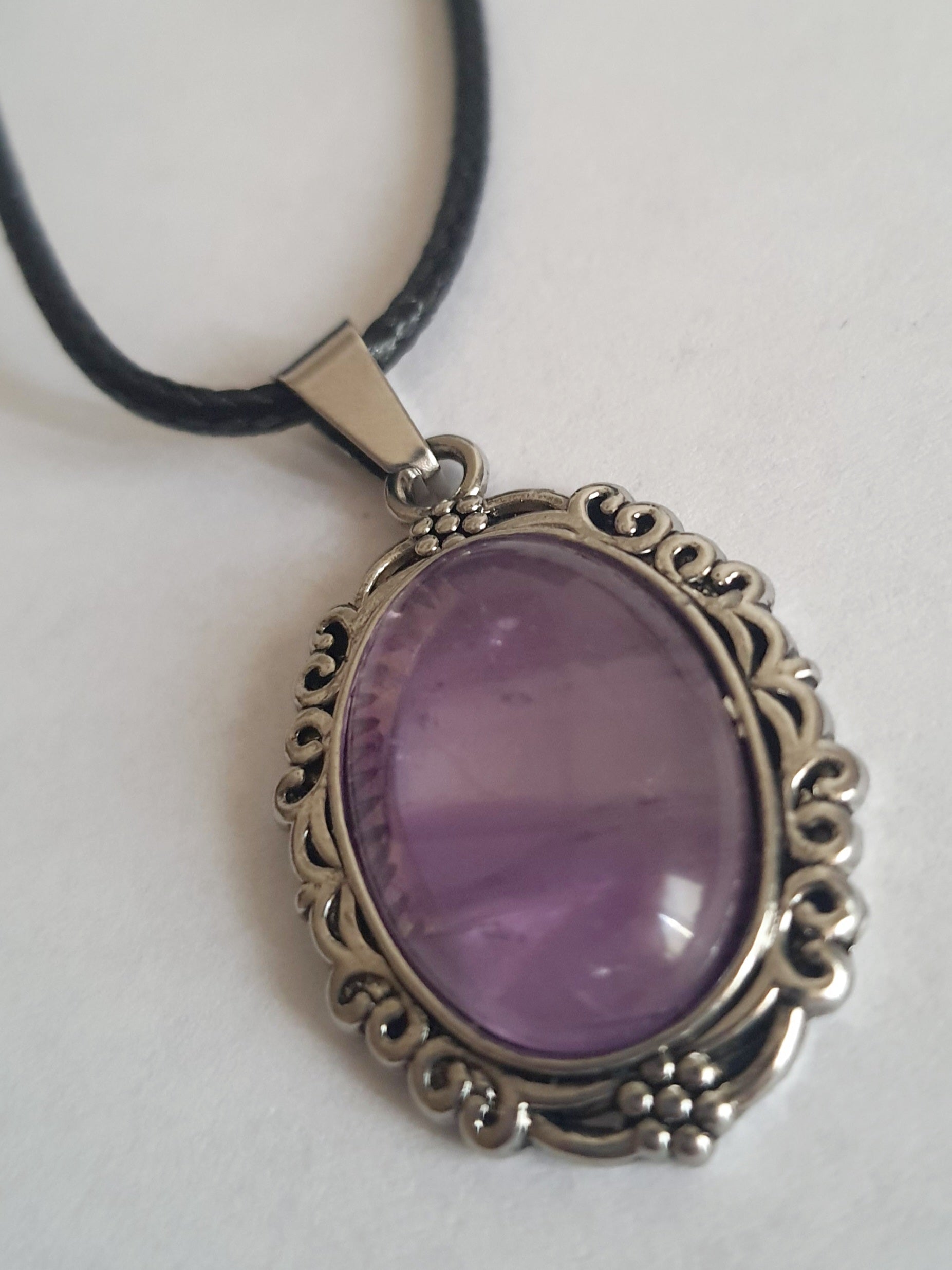Naszyjnik vintage ze stali nierdzewnej – stal chirurgiczna, wodoodporne, hipoalergiczne, jakość premium. Owalna zawieszka z syntetycznym ametystem w ozdobnej ramie. Czarny rzemyk o długości 40–45 cm. Elegancja i styl RougeBizu.