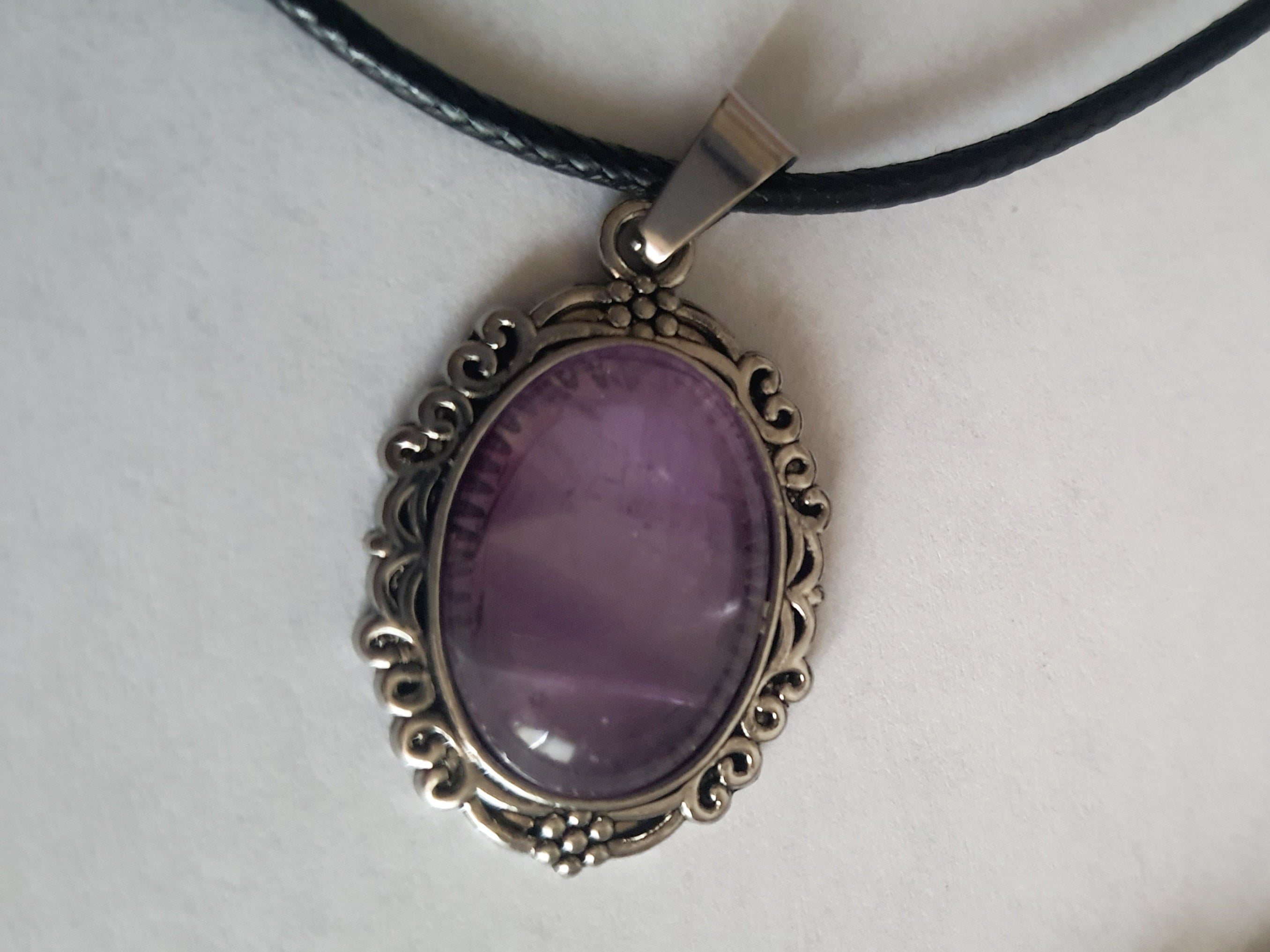 Naszyjnik vintage ze stali nierdzewnej – stal chirurgiczna, wodoodporne, hipoalergiczne, jakość premium. Owalna zawieszka z syntetycznym ametystem w ozdobnej ramie. Czarny rzemyk o długości 40–45 cm. Elegancja i styl RougeBizu.