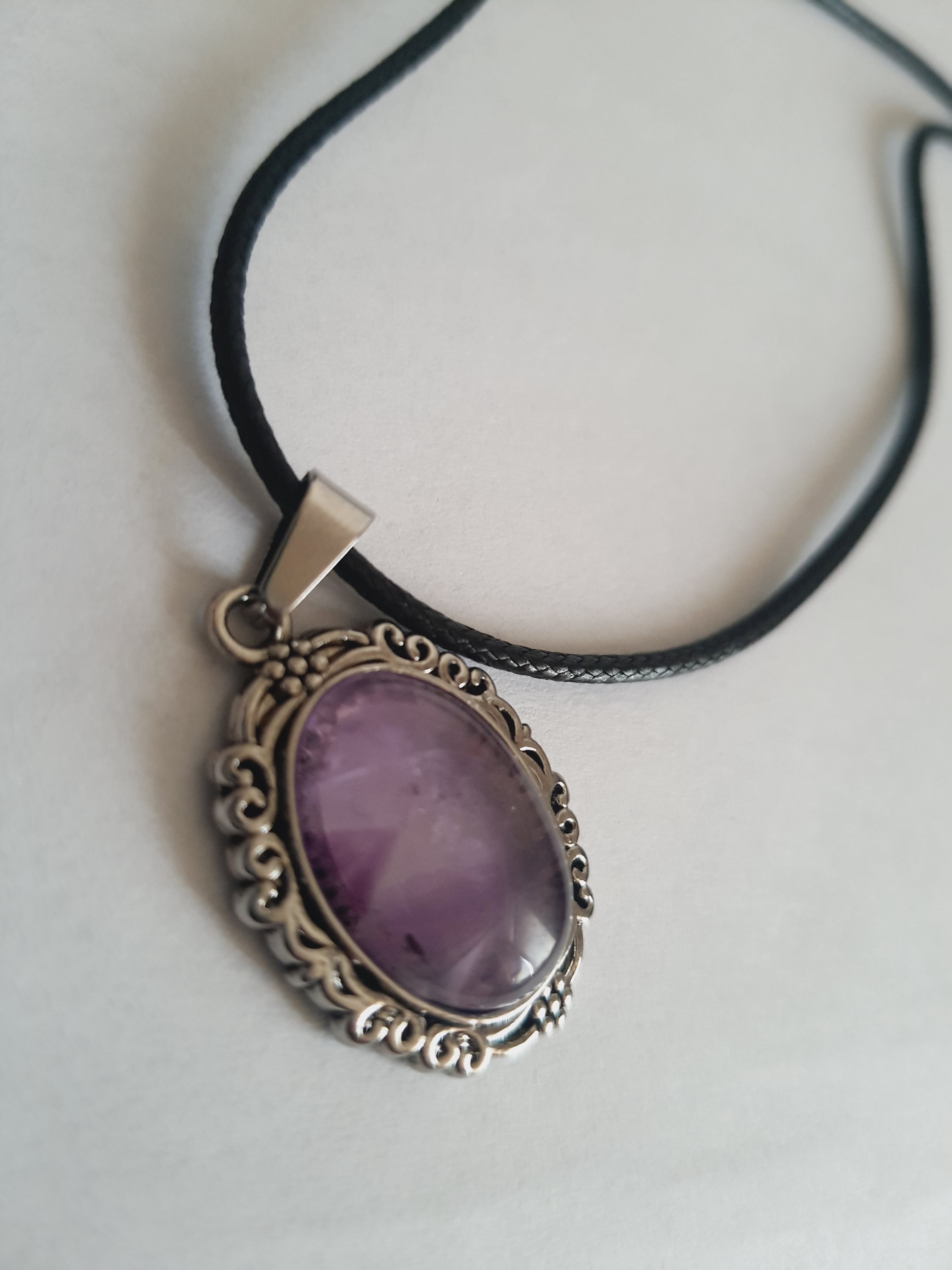 Naszyjnik vintage ze stali nierdzewnej – stal chirurgiczna, wodoodporne, hipoalergiczne, jakość premium. Owalna zawieszka z syntetycznym ametystem w ozdobnej ramie. Czarny rzemyk o długości 40–45 cm. Elegancja i styl RougeBizu.