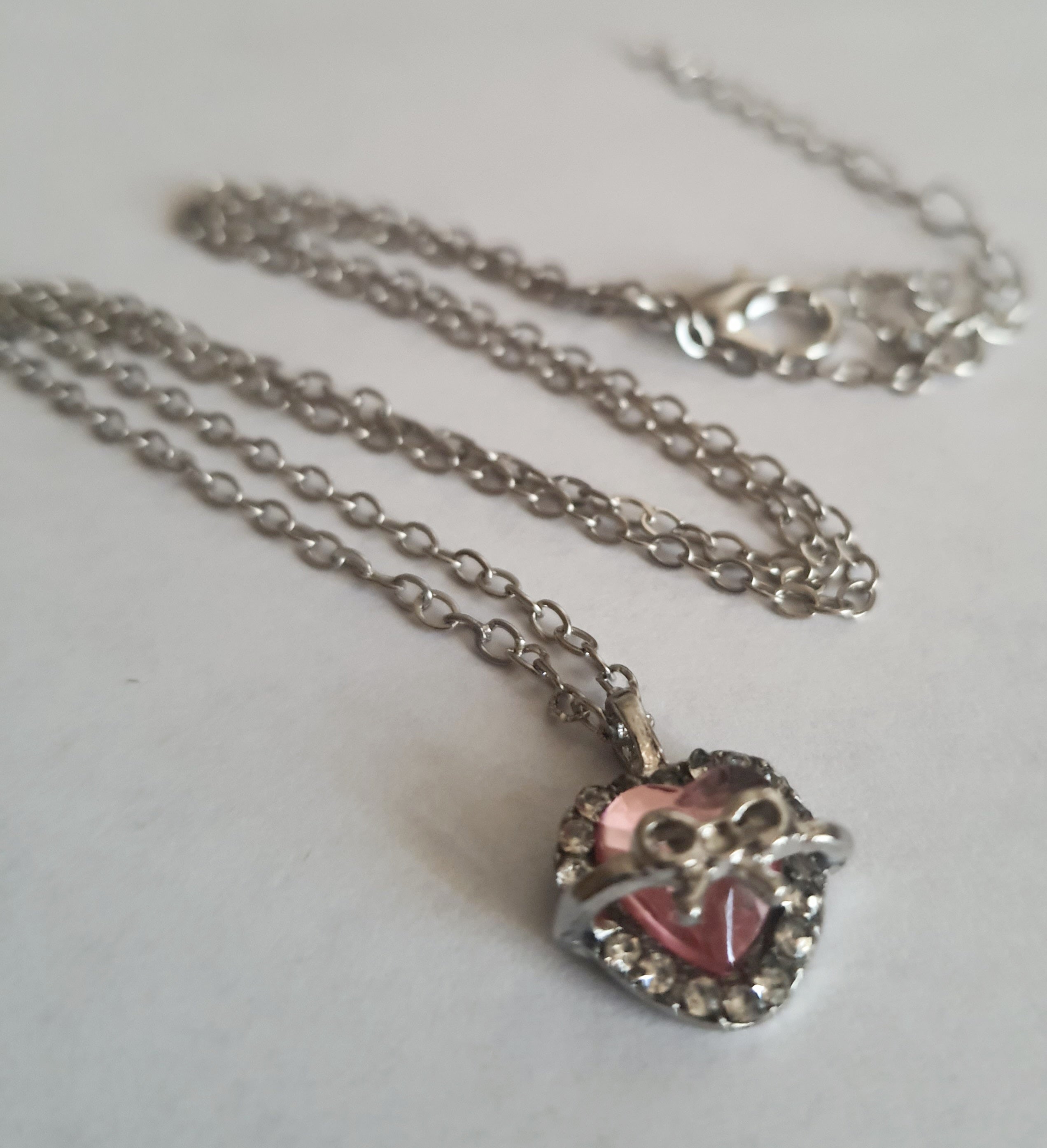 Srebrny naszyjnik ze stali nierdzewnej – stal chirurgiczna, wodoodporny, hipoalergiczny, jakość premium. Zawieszka w kształcie różowego serca z kokardką i otoczką z cyrkonii. Długość łańcuszka 42–49 cm. RougeBizu.