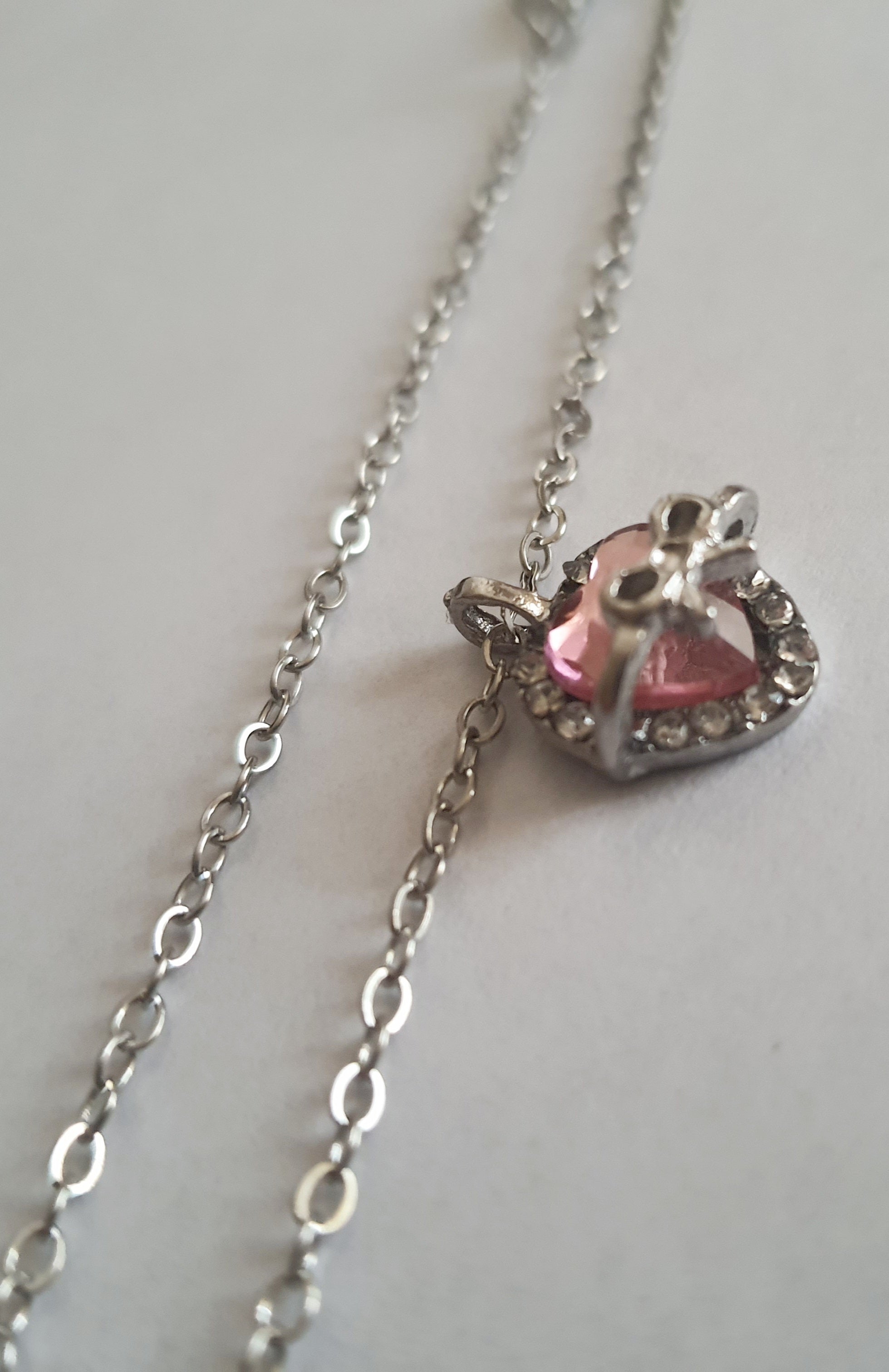 Srebrny naszyjnik ze stali nierdzewnej – stal chirurgiczna, wodoodporny, hipoalergiczny, jakość premium. Zawieszka w kształcie różowego serca z kokardką i otoczką z cyrkonii. Długość łańcuszka 42–49 cm. RougeBizu.