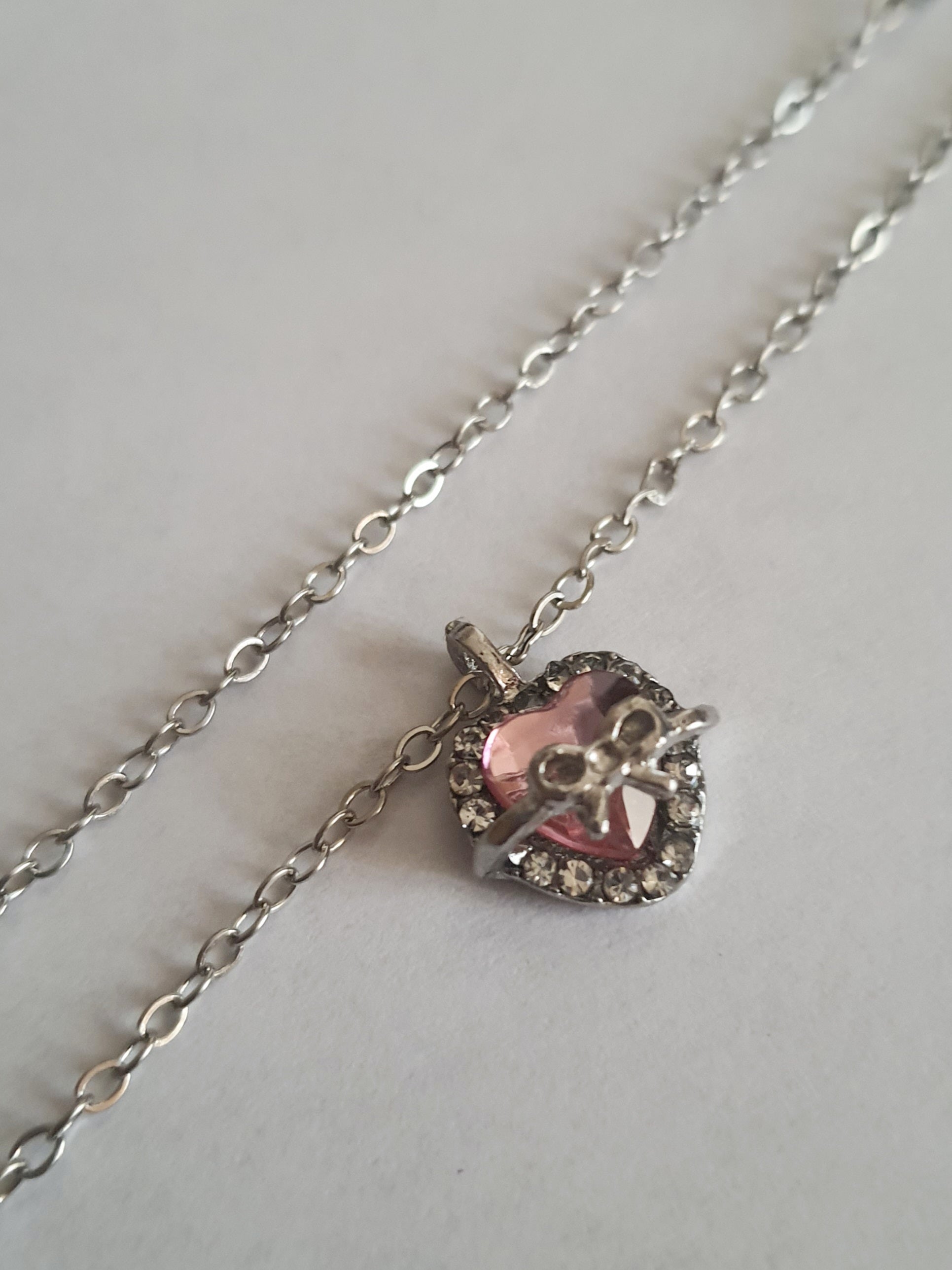 Srebrny naszyjnik ze stali nierdzewnej – stal chirurgiczna, wodoodporny, hipoalergiczny, jakość premium. Zawieszka w kształcie różowego serca z kokardką i otoczką z cyrkonii. Długość łańcuszka 42–49 cm. RougeBizu.