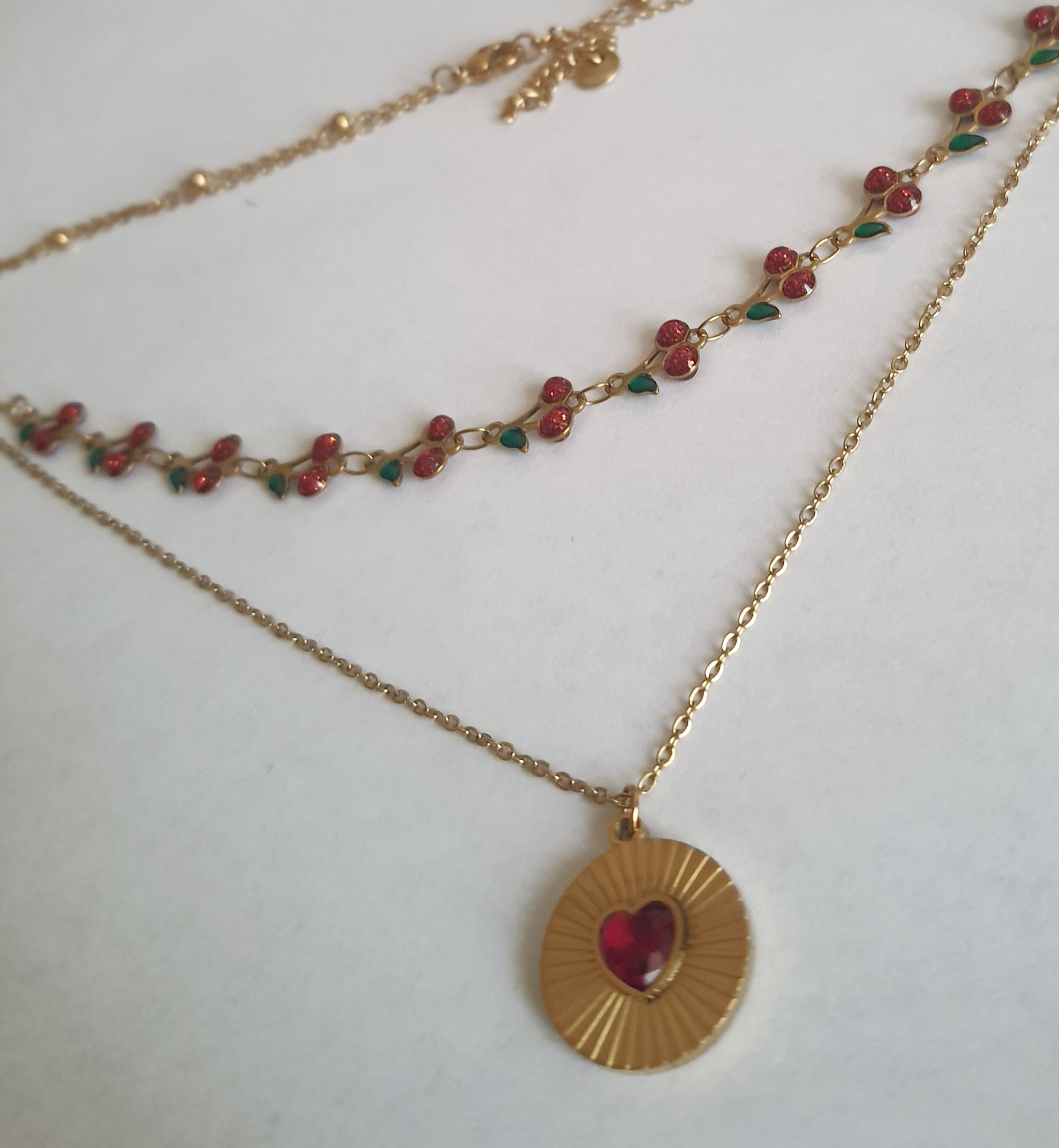 Podwójny złoty naszyjnik ze stali nierdzewnej – stal chirurgiczna, wodoodporny, hipoalergiczny, jakość premium. Pierwsza warstwa z czerwonymi wiśniami i zielonymi listkami, druga z medalionem i czerwonym sercem. Długość 40–50 cm. RougeBizu.