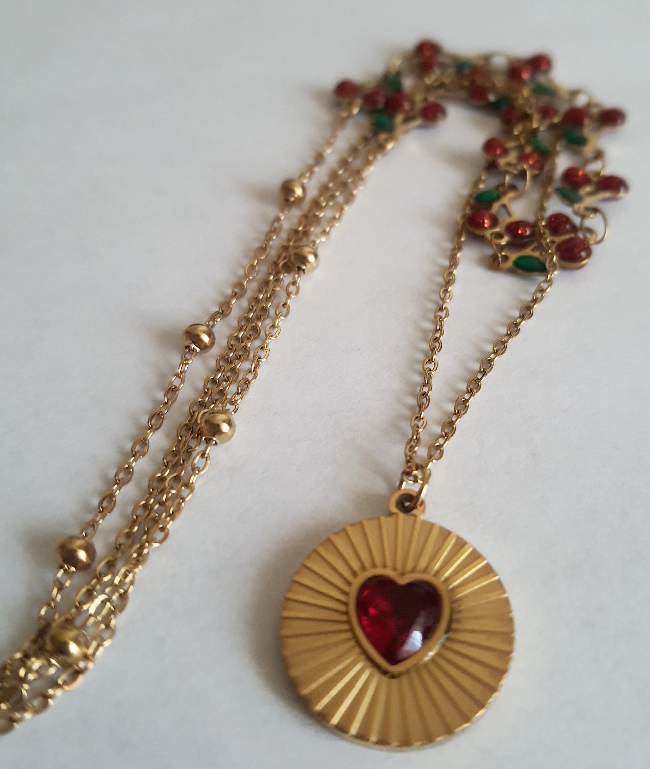 Podwójny złoty naszyjnik ze stali nierdzewnej – stal chirurgiczna, wodoodporny, hipoalergiczny, jakość premium. Pierwsza warstwa z czerwonymi wiśniami i zielonymi listkami, druga z medalionem i czerwonym sercem. Długość 40–50 cm. RougeBizu.