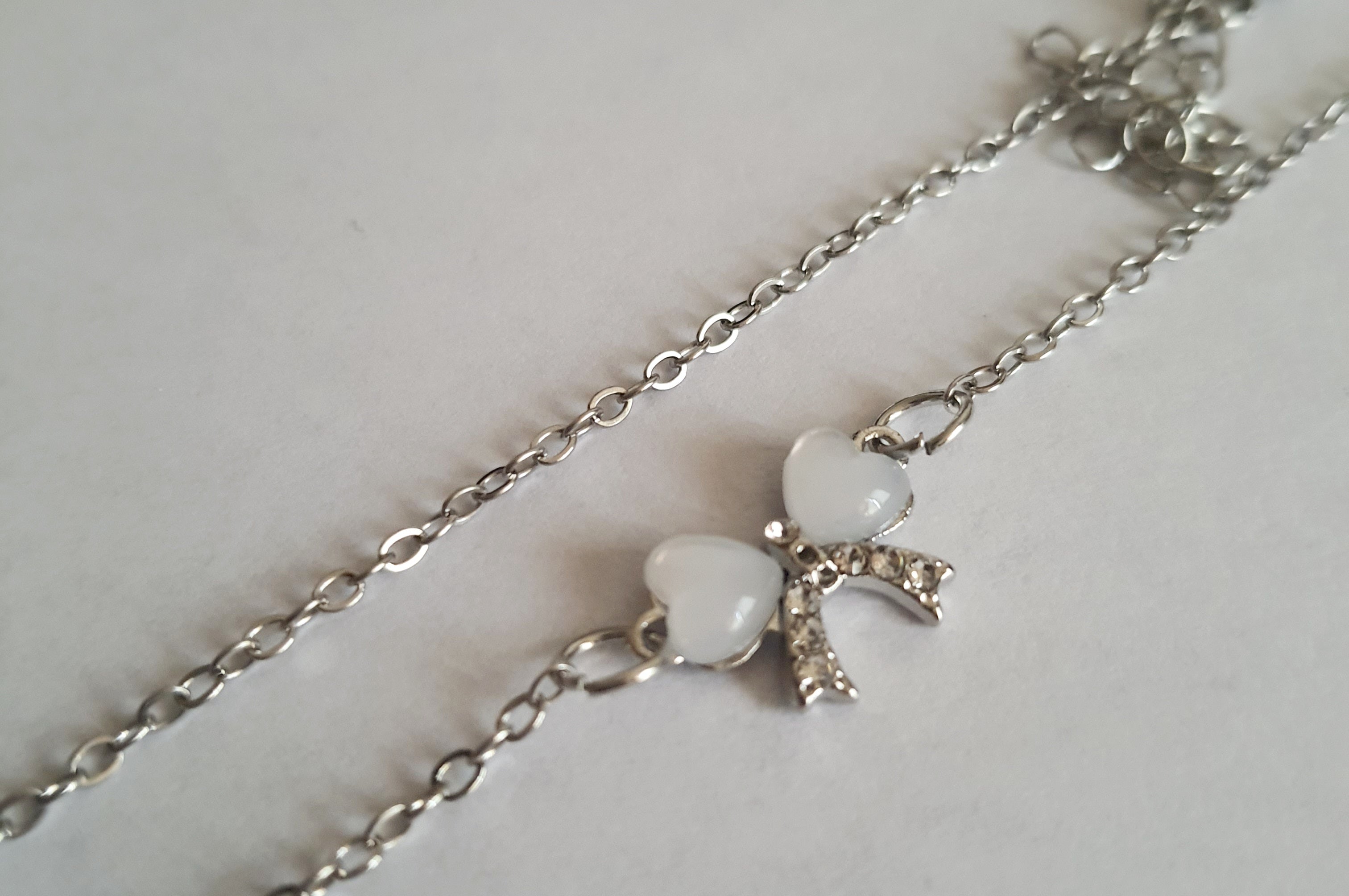 Srebrny naszyjnik ze stali nierdzewnej – stal chirurgiczna, wodoodporny, hipoalergiczny, jakość premium. Zawieszka w kształcie kokardki z dwóch serc, zdobiona kryształkami. Długość łańcuszka 42–49 cm. RougeBizu.