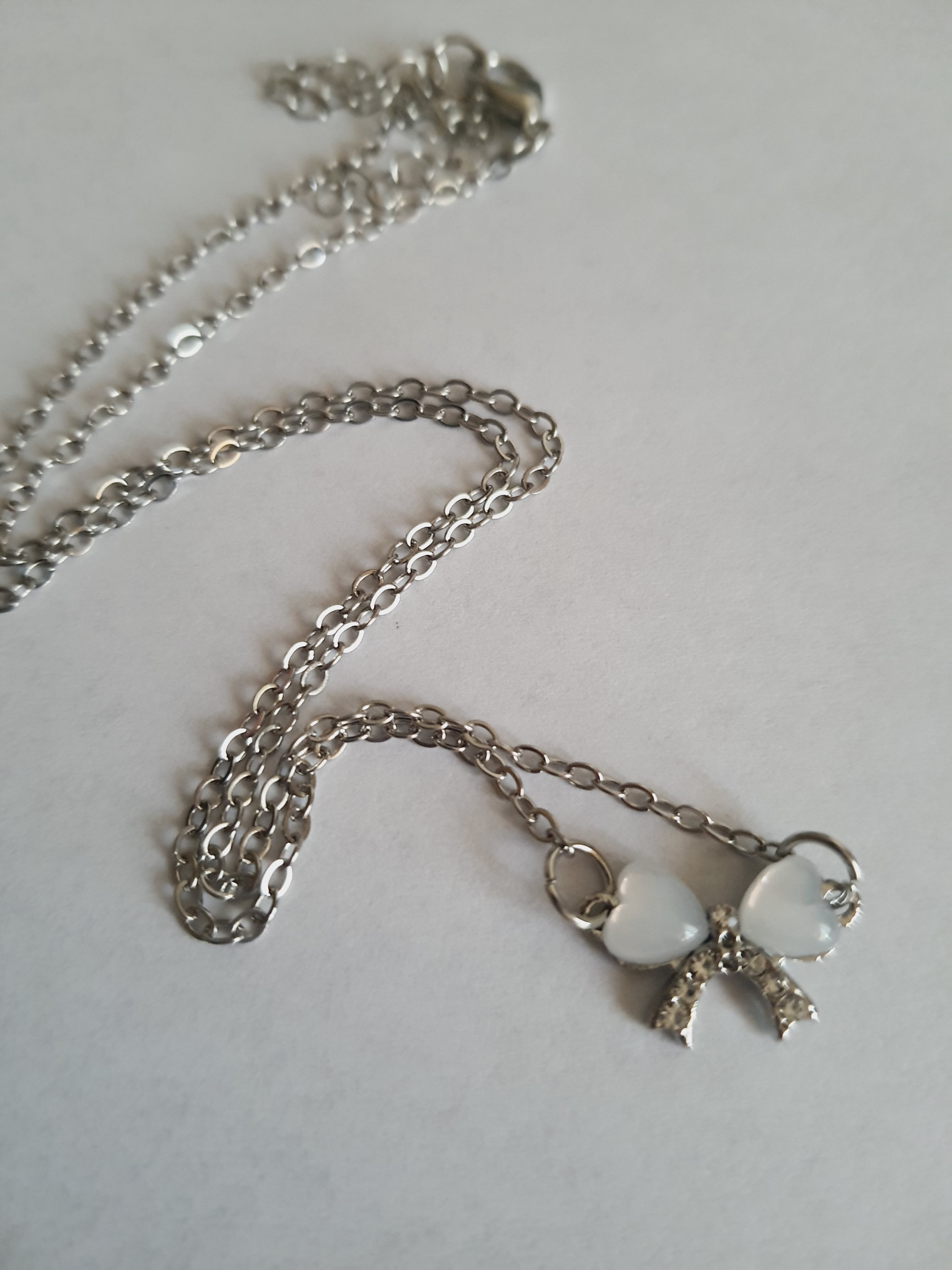 Srebrny naszyjnik ze stali nierdzewnej – stal chirurgiczna, wodoodporny, hipoalergiczny, jakość premium. Zawieszka w kształcie kokardki z dwóch serc, zdobiona kryształkami. Długość łańcuszka 42–49 cm. RougeBizu.