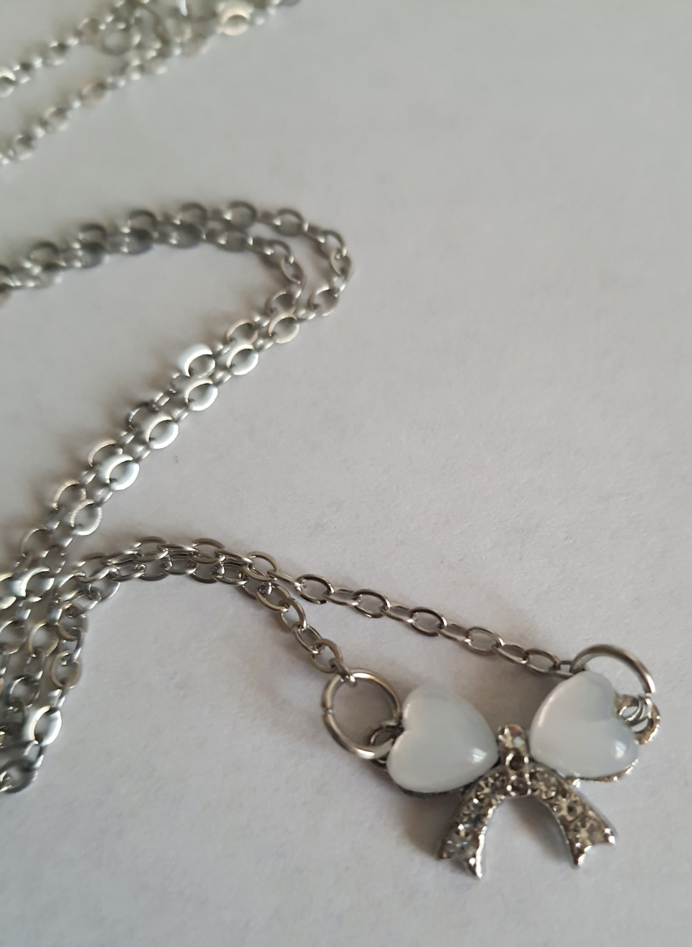 Srebrny naszyjnik ze stali nierdzewnej – stal chirurgiczna, wodoodporny, hipoalergiczny, jakość premium. Zawieszka w kształcie kokardki z dwóch serc, zdobiona kryształkami. Długość łańcuszka 42–49 cm. RougeBizu.