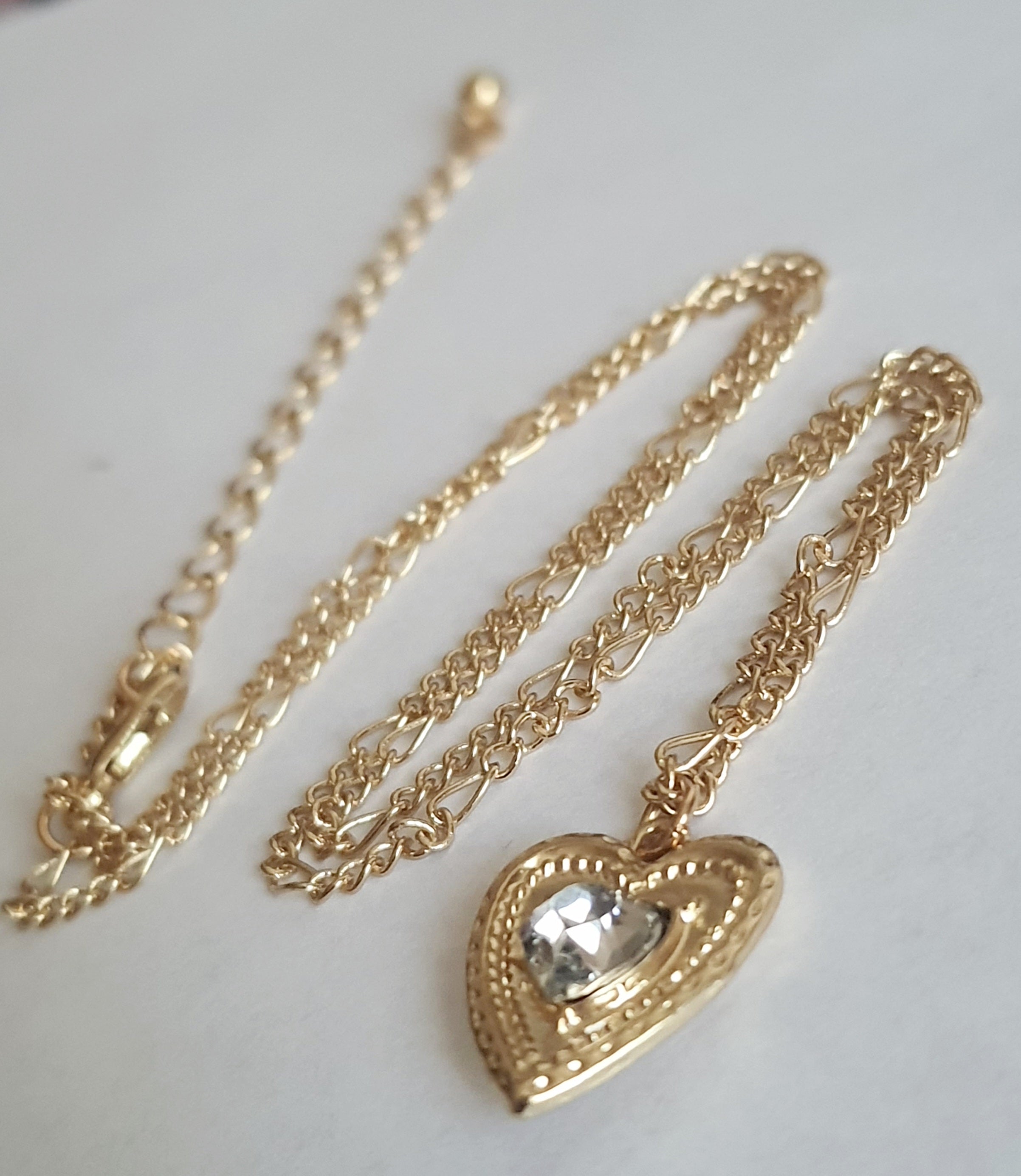 Złoty naszyjnik ze stali chirurgicznej, łańcuszek 43–50 cm, zawieszka w kształcie serca z centralnym kryształem, elegancja i romantyczny styl. Stal nierdzewna, wodoodporne, hipoalergiczne, jakość premium. Rouge Bizu.