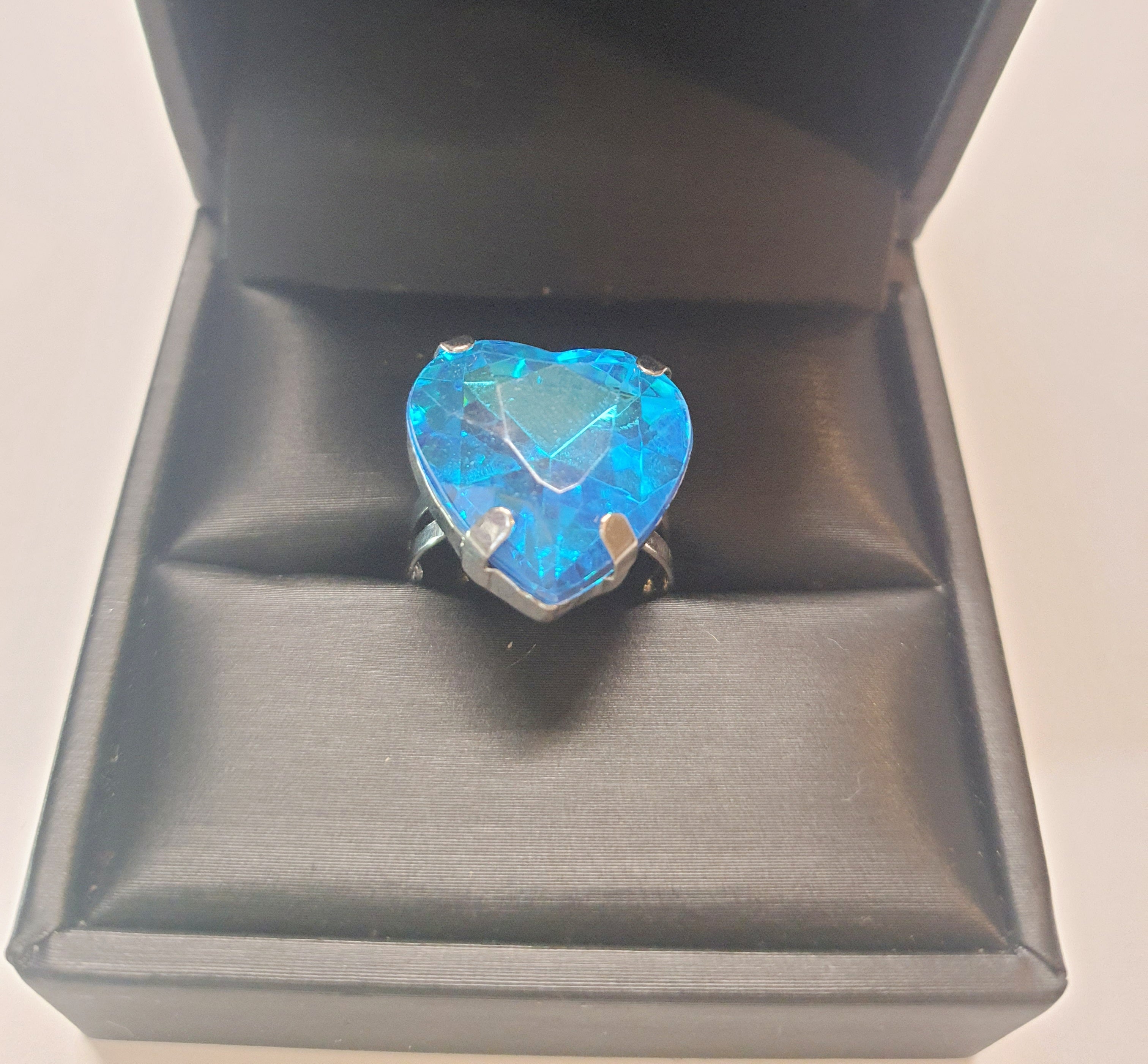 Srebrny pierścionek z dużym niebieskim kamieniem w kształcie serca, metal, szlifowany kamień o morskim odcieniu, styl romantyczny glamour, regulowany rozmiar, Rouge Bizu.