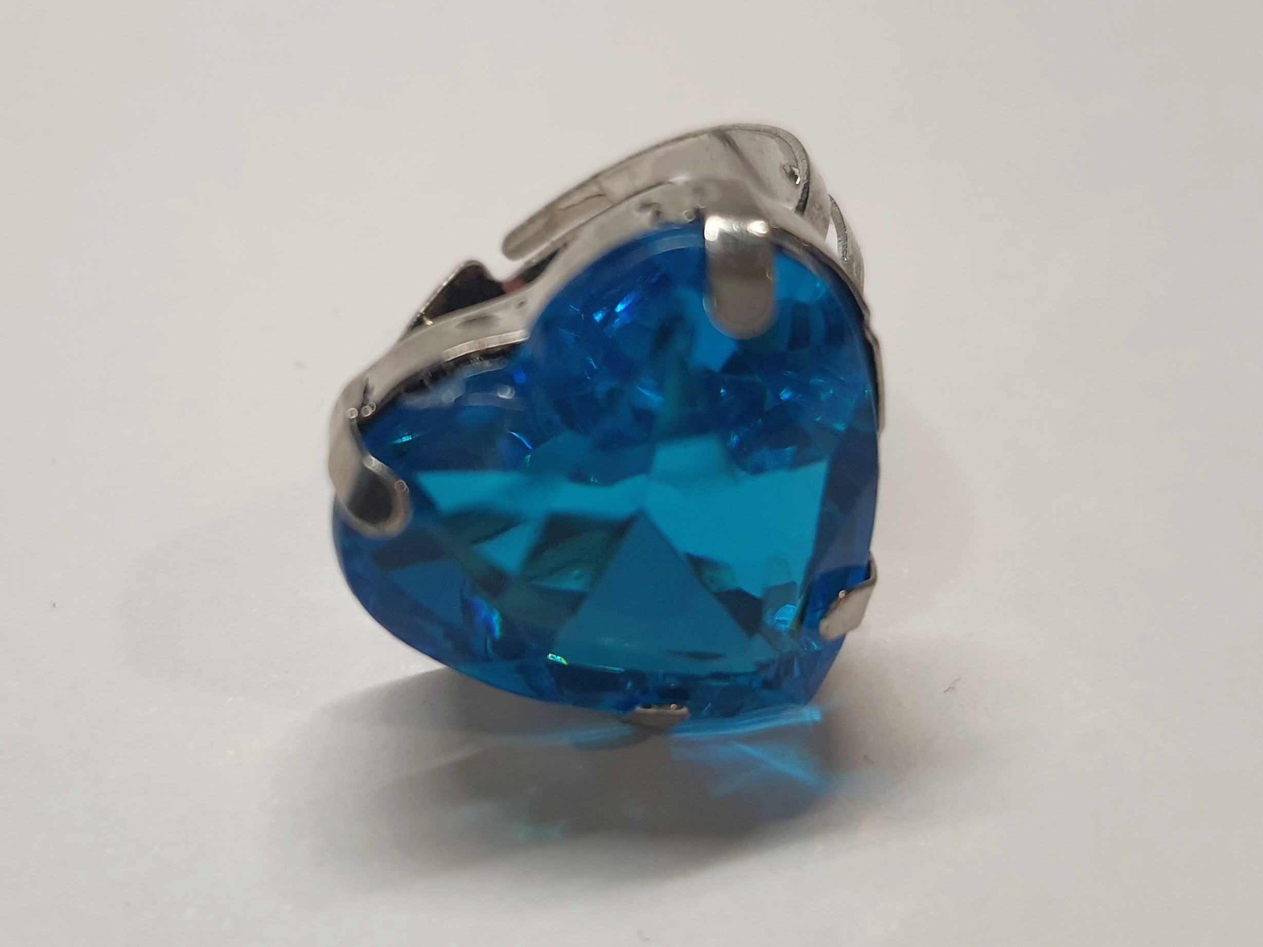 Srebrny pierścionek z dużym niebieskim kamieniem w kształcie serca, metal, szlifowany kamień o morskim odcieniu, styl romantyczny glamour, regulowany rozmiar, Rouge Bizu.