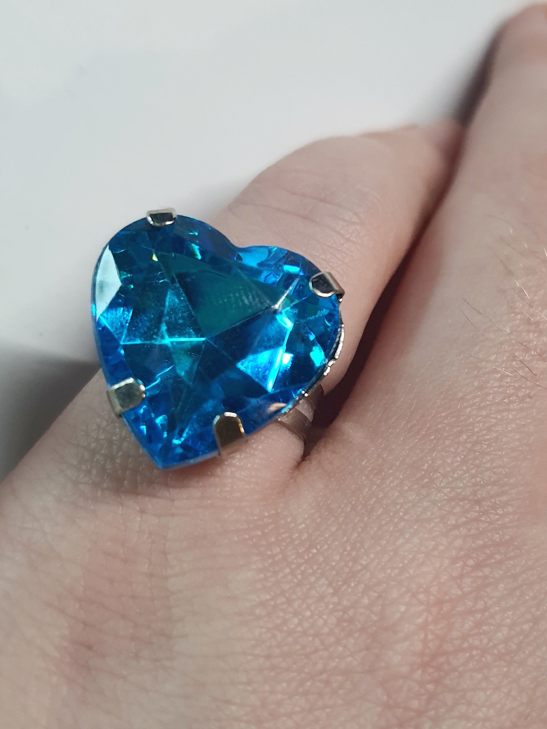 Srebrny pierścionek z dużym niebieskim kamieniem w kształcie serca, metal, szlifowany kamień o morskim odcieniu, styl romantyczny glamour, regulowany rozmiar, Rouge Bizu.