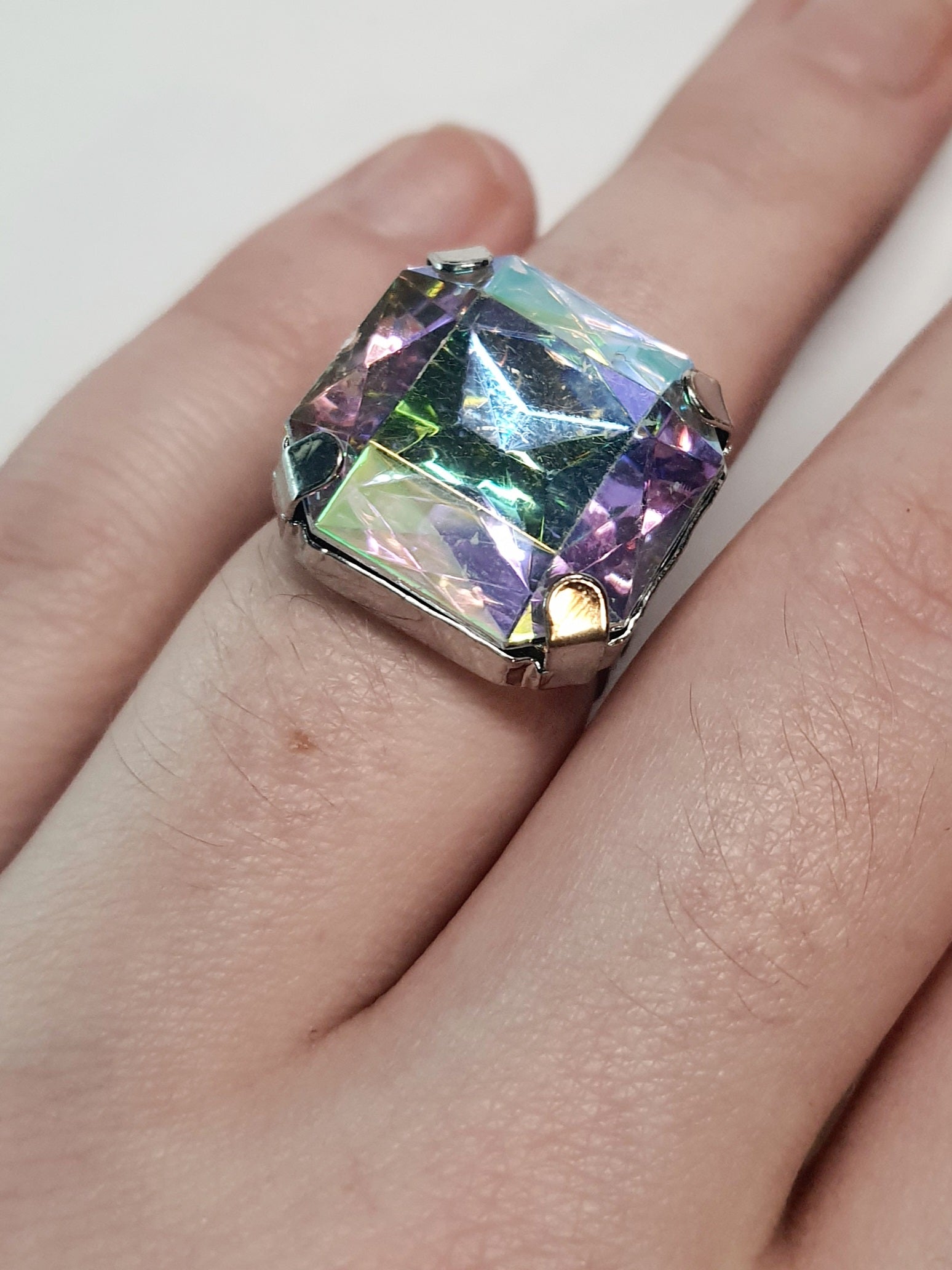 Srebrny pierścionek z dużym wielokolorowym prostokątnym kamieniem, metal, szlifowany kamień o tęczowym połysku, styl glamour, regulowany rozmiar, Rouge Bizu.