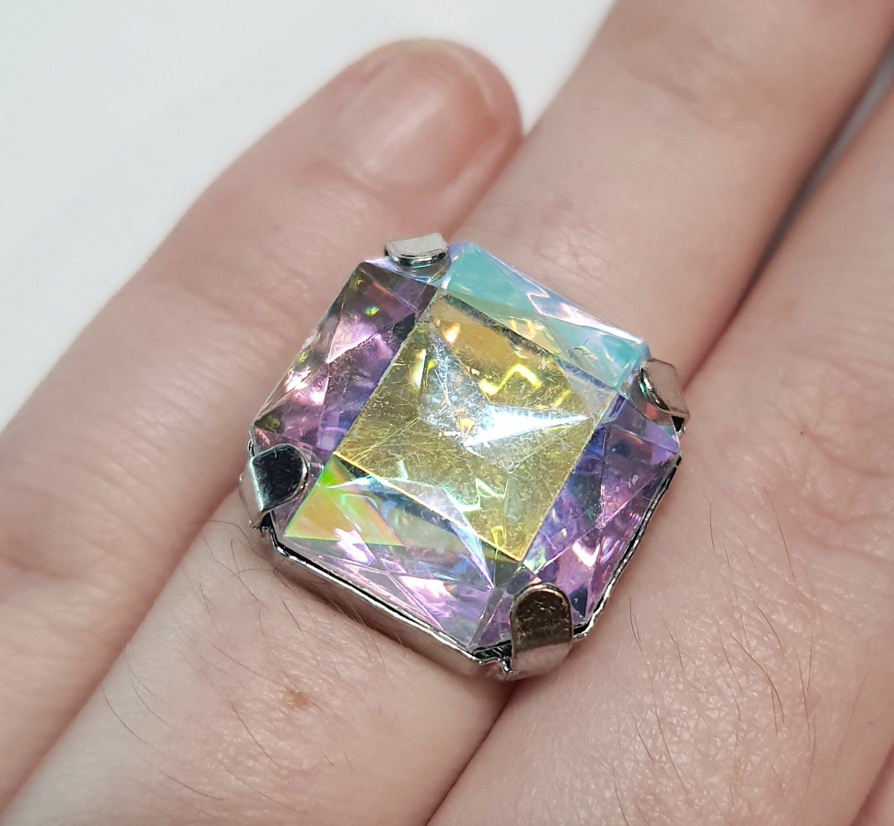 Srebrny pierścionek z dużym wielokolorowym prostokątnym kamieniem, metal, szlifowany kamień o tęczowym połysku, styl glamour, regulowany rozmiar, Rouge Bizu.