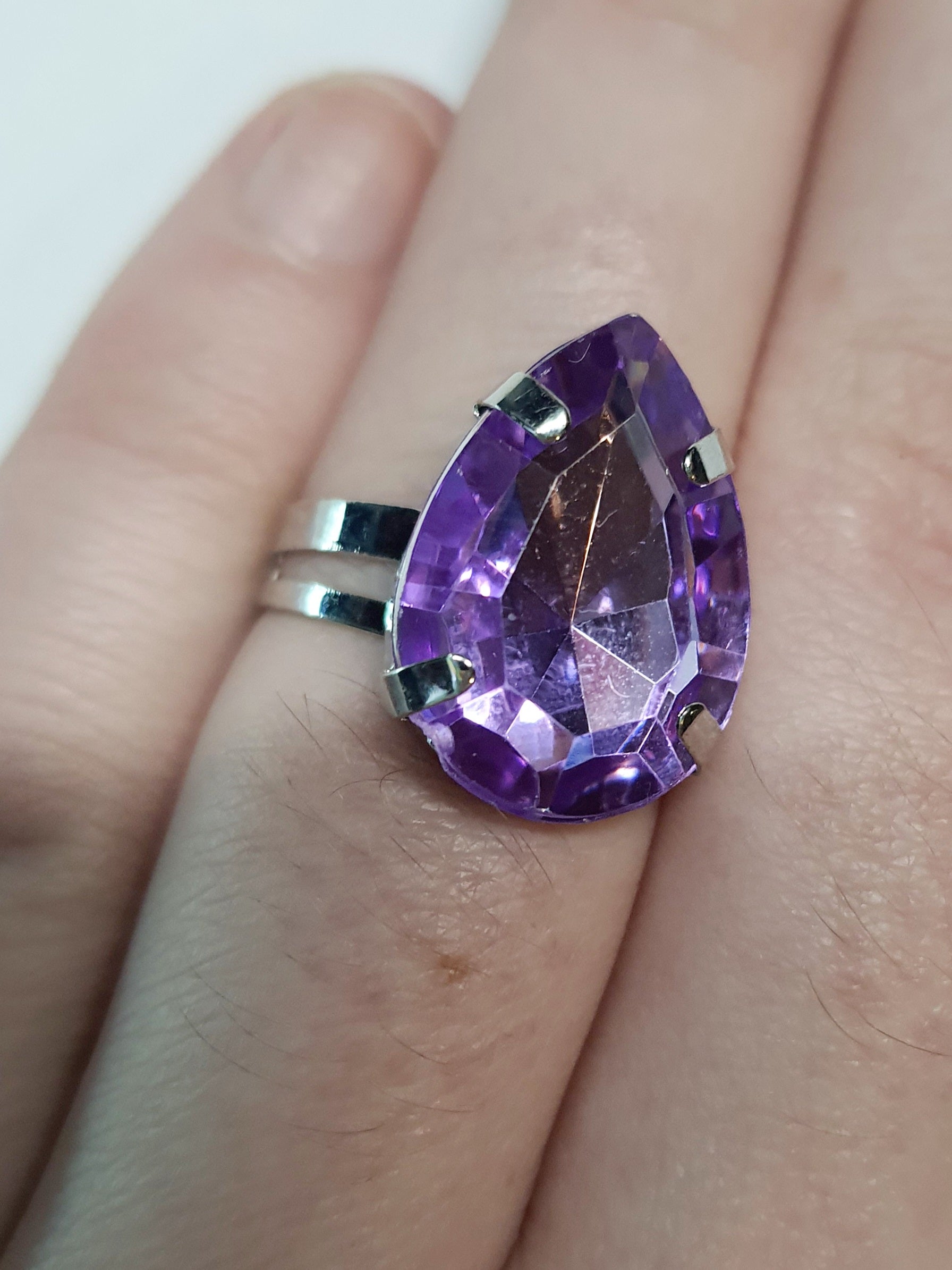 Srebrny pierścionek z dużym fioletowym kamieniem w kształcie łezki, metal, szlifowany kamień o głębokim połysku, elegancki styl, regulowany rozmiar, Rouge Bizu.