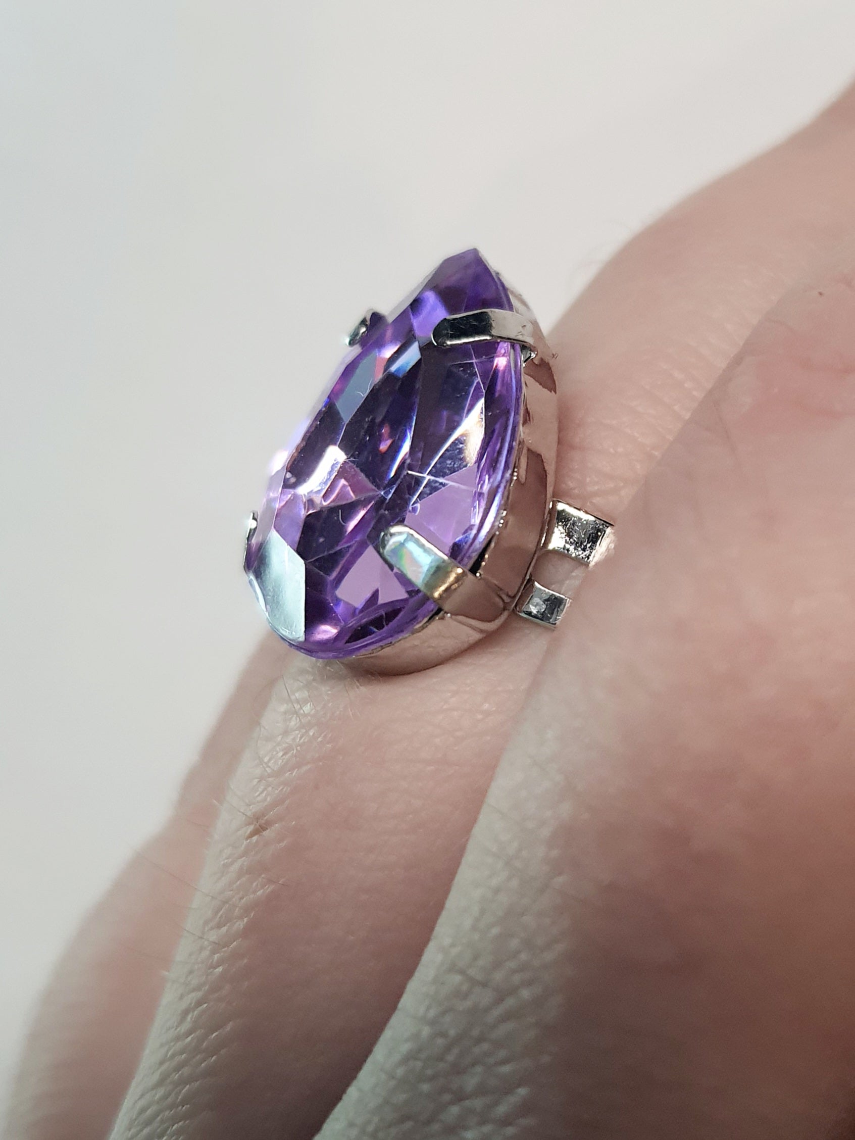 Srebrny pierścionek z dużym fioletowym kamieniem w kształcie łezki, metal, szlifowany kamień o głębokim połysku, elegancki styl, regulowany rozmiar, Rouge Bizu.