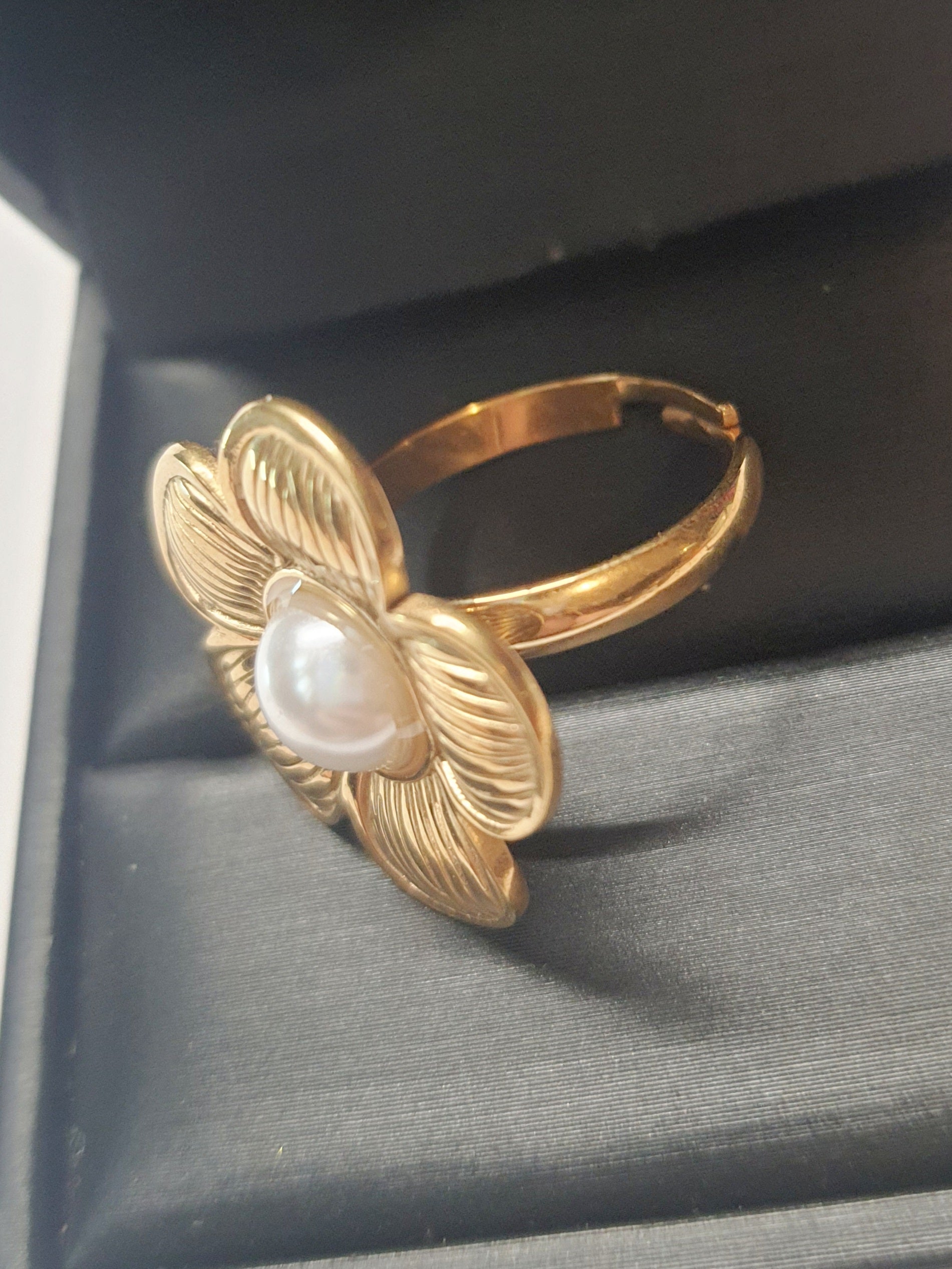 Złoty pierścionek w kształcie kwiatu z białą perłą w centrum, elegancki i kobiecy. Rozmiar 17 mm, regulowany. Stal nierdzewna, stal chirurgiczna, wodoodporne, hipoalergiczne, jakość premium. Rouge Bizu.