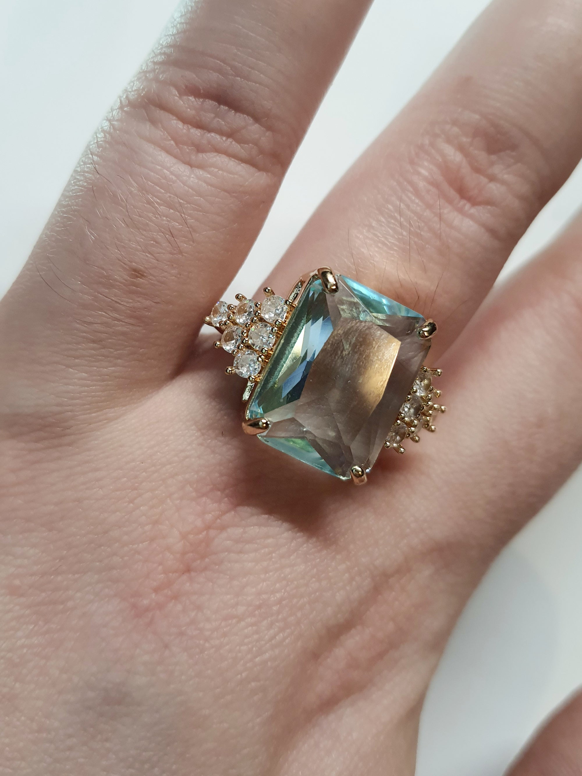 Złoty pierścionek ze stali nierdzewnej z prostokątnym błękitnym kamieniem i cyrkoniami po bokach w stylu glamour klasycznym. Rozmiar 20 mm. stal chirurgiczna, stal nierdzewna, wodoodporne, hipoalergiczne, jakość premium, RougeBizu.