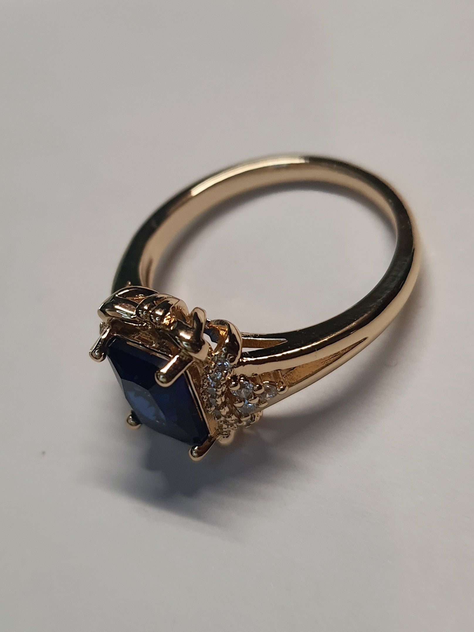 Złoty pierścionek ze stali nierdzewnej z granatowym kamieniem w szlifie szmaragdowym i cyrkoniami po bokach w stylu glamour klasycznym. Rozmiar 20 mm. stal chirurgiczna, stal nierdzewna, wodoodporne, hipoalergiczne, jakość premium, RougeBizu.