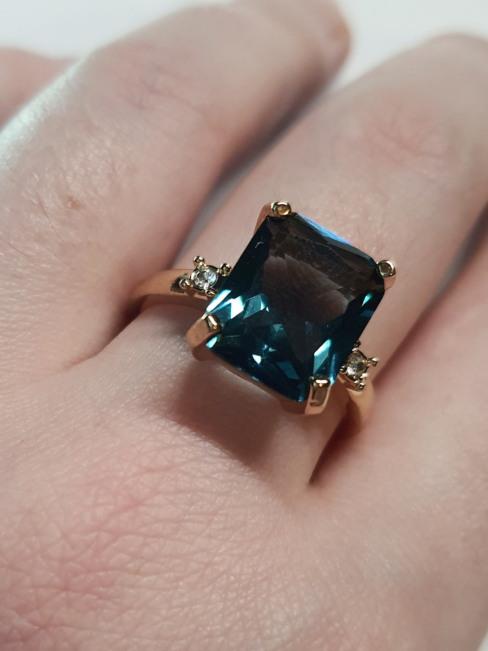 Złoty pierścionek ze stali nierdzewnej z prostokątnym szafirowym kamieniem i drobnymi cyrkoniami po bokach w stylu klasycznym glamour. Rozmiar 19 mm. stal chirurgiczna, stal nierdzewna, wodoodporne, hipoalergiczne, jakość premium, RougeBizu.