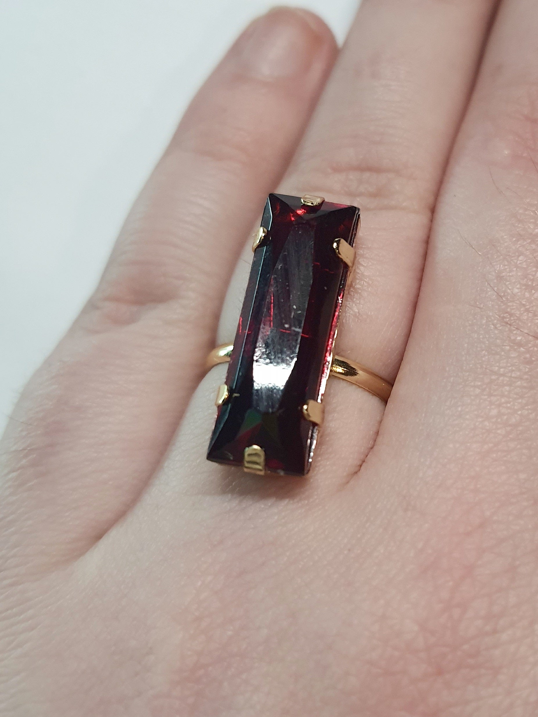 Złoty pierścionek z długim rubinowym kamieniem w stylu glamour, elegancki i efektowny. Rozmiar 17 mm, lekko regulowany. Stal nierdzewna, stal chirurgiczna, wodoodporne, hipoalergiczne, jakość premium. Rouge Bizu.