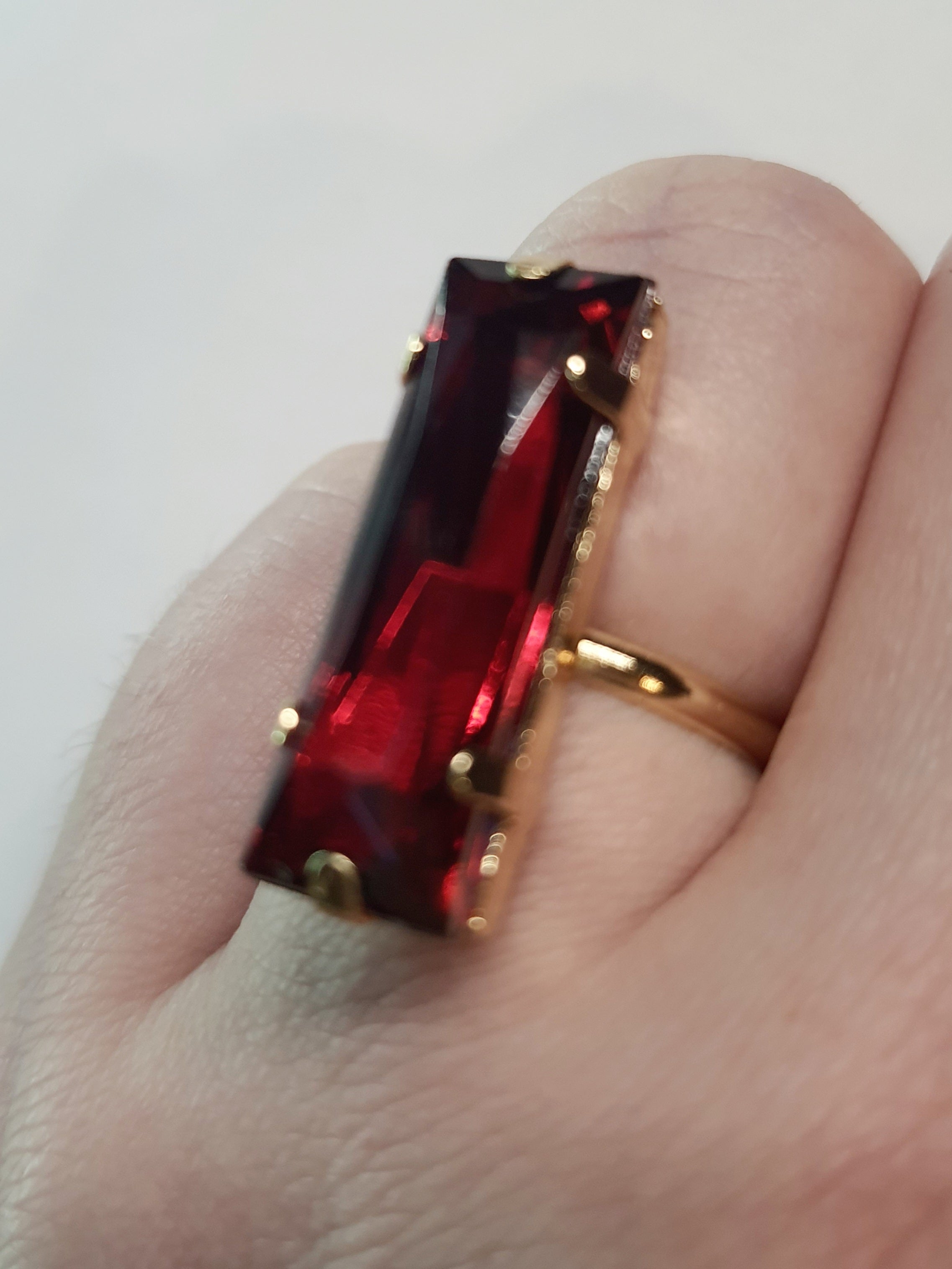 Złoty pierścionek z długim rubinowym kamieniem w stylu glamour, elegancki i efektowny. Rozmiar 17 mm, lekko regulowany. Stal nierdzewna, stal chirurgiczna, wodoodporne, hipoalergiczne, jakość premium. Rouge Bizu.