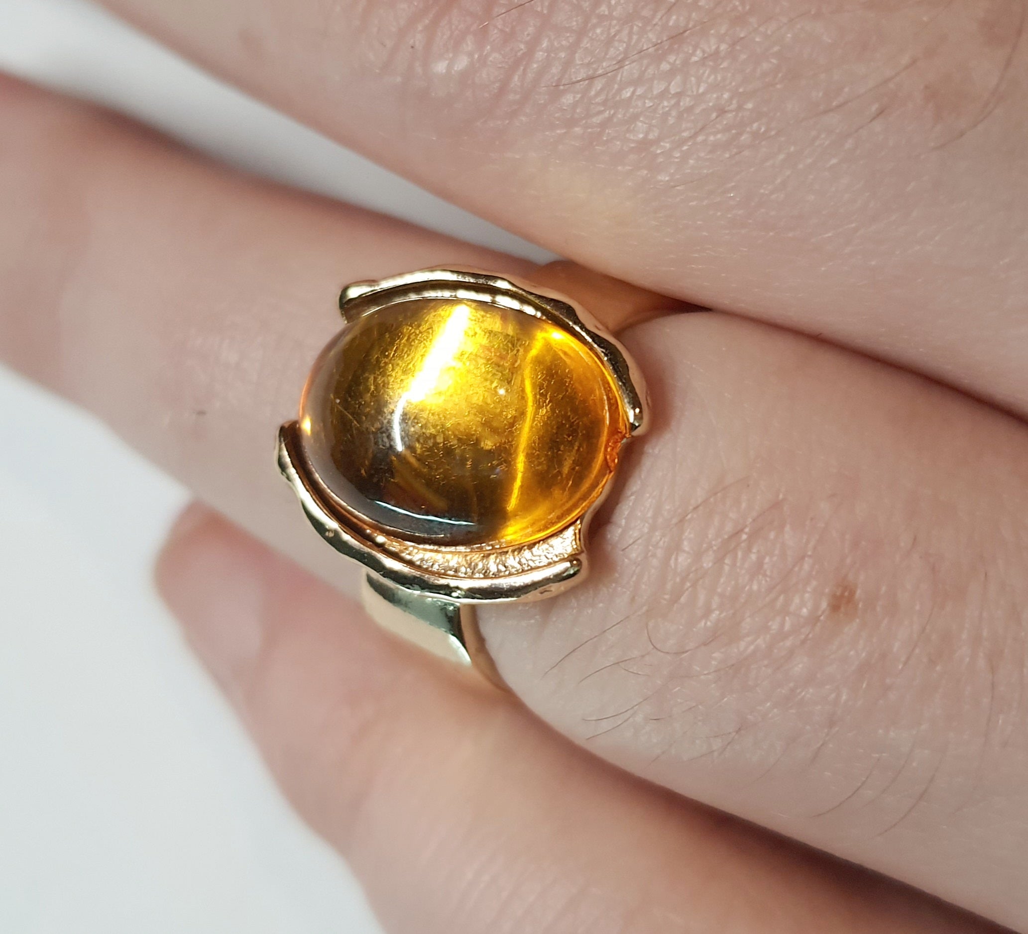 Złoty pierścionek ze stali nierdzewnej z owalnym bursztynowym kamieniem w artystycznej oprawie o nieregularnej formie. Rozmiar 16 mm. stal chirurgiczna, stal nierdzewna, wodoodporne, hipoalergiczne, jakość premium, RougeBizu.