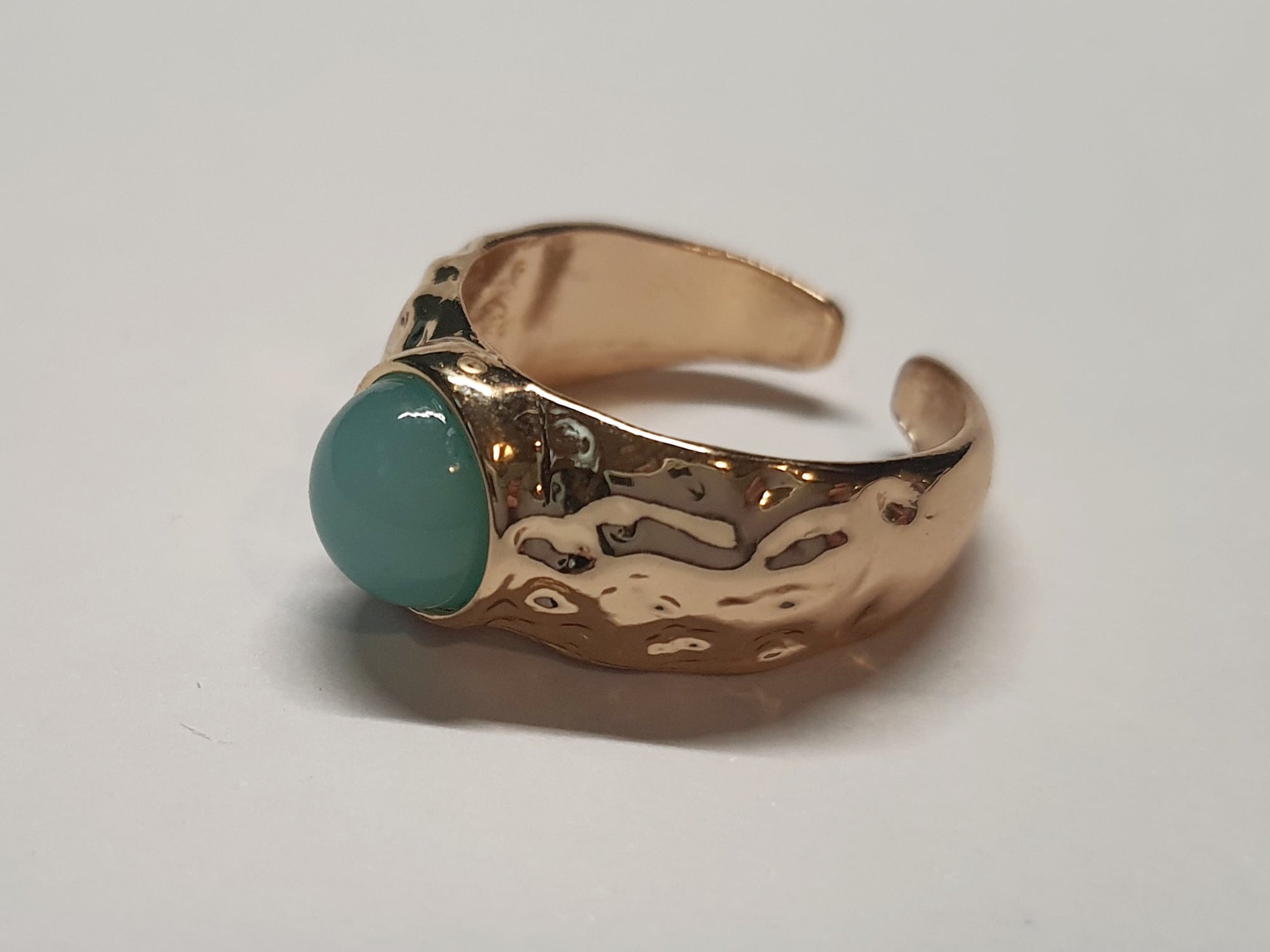 Złoty pierścionek z mleczno–turkusowym kamieniem w młotkowanej oprawie, elegancki i nowoczesny. Rozmiar 17 mm, regulowany. Stal nierdzewna, stal chirurgiczna, wodoodporne, hipoalergiczne, jakość premium. Rouge Bizu.