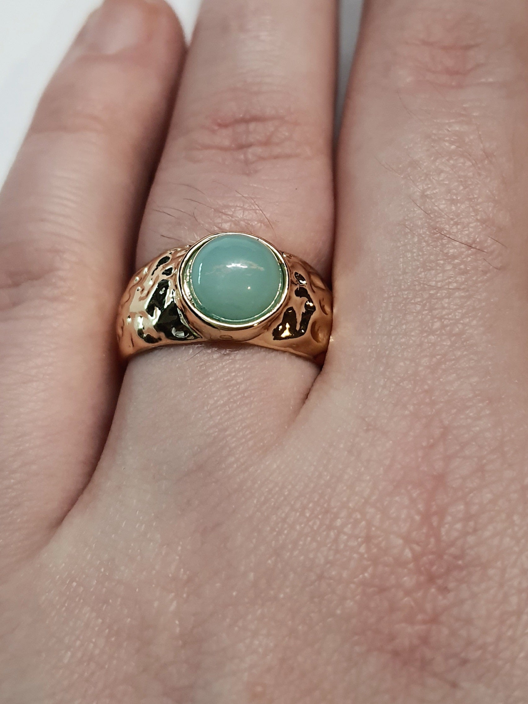 Złoty pierścionek z mleczno–turkusowym kamieniem w młotkowanej oprawie, elegancki i nowoczesny. Rozmiar 17 mm, regulowany. Stal nierdzewna, stal chirurgiczna, wodoodporne, hipoalergiczne, jakość premium. Rouge Bizu.