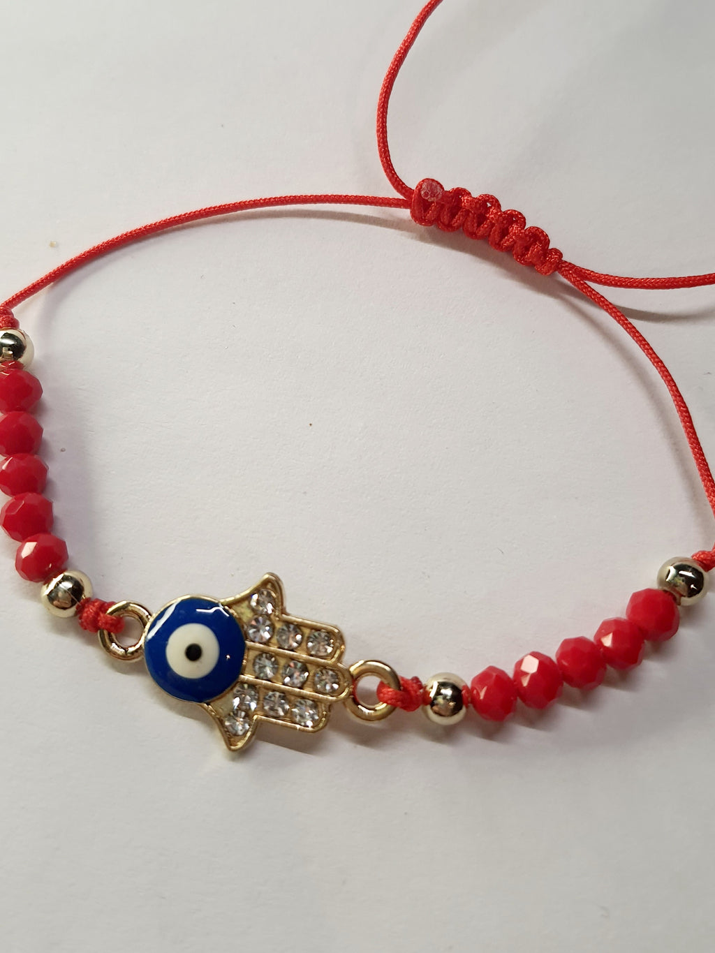 Bransoletka na czerwonym sznurku z zawieszką w kształcie dłoni Fatimy z okiem proroka, zdobioną cyrkoniami. Styl boho i amulet ochronny. Stal chirurgiczna, stal nierdzewna, wodoodporne, hipoalergiczne, jakość premium. Rouge Bizu.