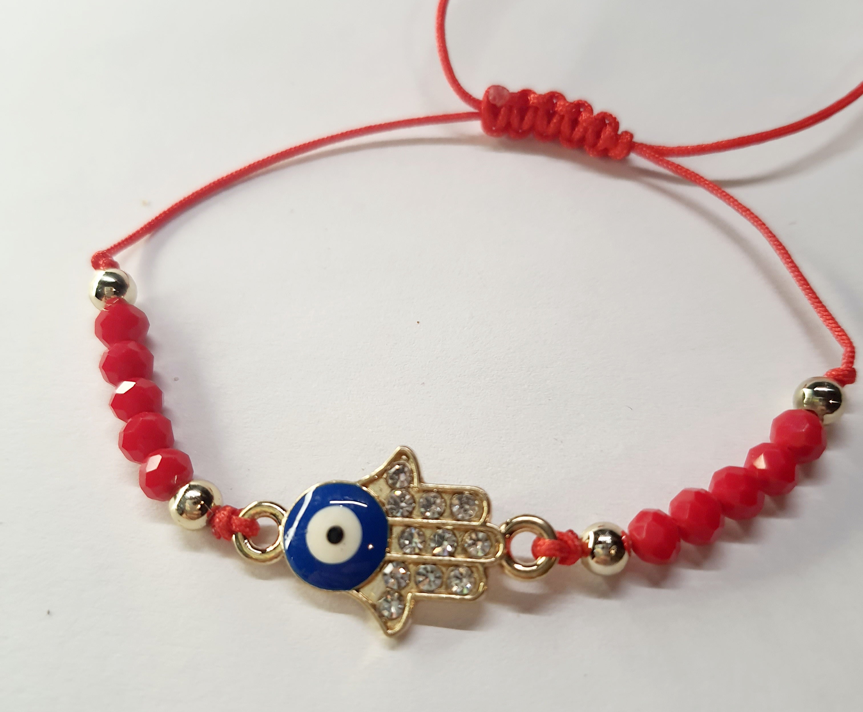 Bransoletka na czerwonym sznurku z zawieszką w kształcie dłoni Fatimy z okiem proroka, zdobioną cyrkoniami. Styl boho i amulet ochronny. Stal chirurgiczna, stal nierdzewna, wodoodporne, hipoalergiczne, jakość premium. Rouge Bizu.