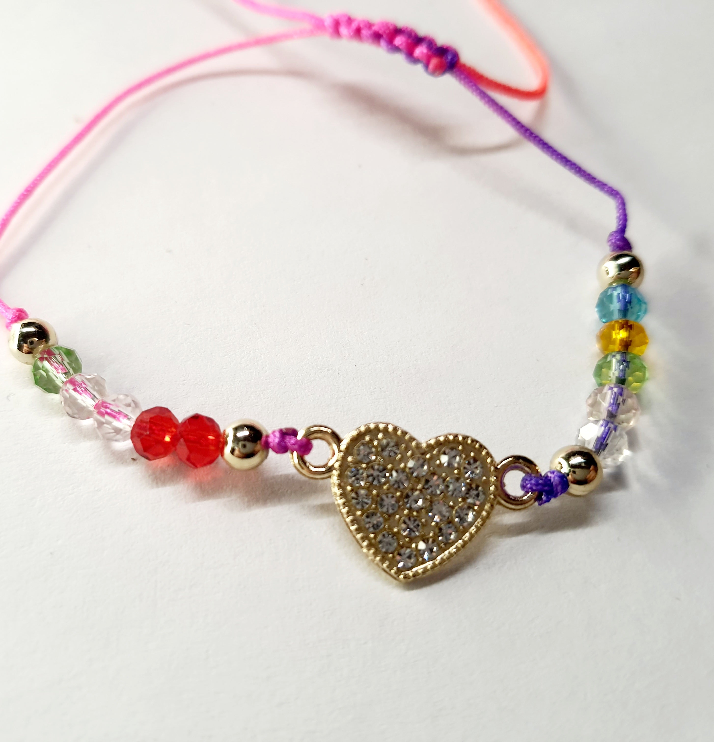 Bransoletka z sercem wysadzanym cyrkoniami na różowo-fioletowym sznurku z kolorowymi koralikami. Delikatna, kolorowa biżuteria w stylu boho, romantyczna i radosna. Wodoodporne, hipoalergiczne, jakość premium. Rouge Bizu.